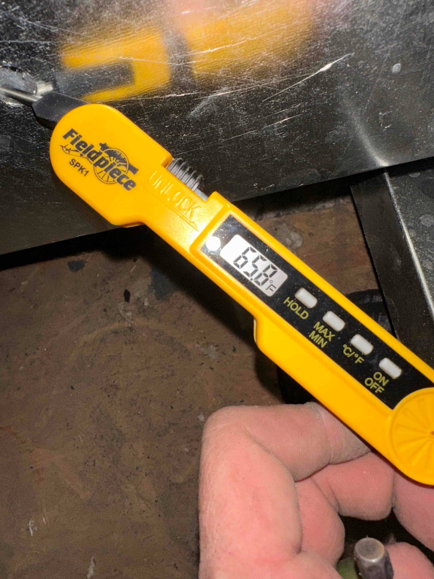 Digital thermometer probe inserted into ductwork shows 65.6 degrees, documenting air temperature during commissioning.