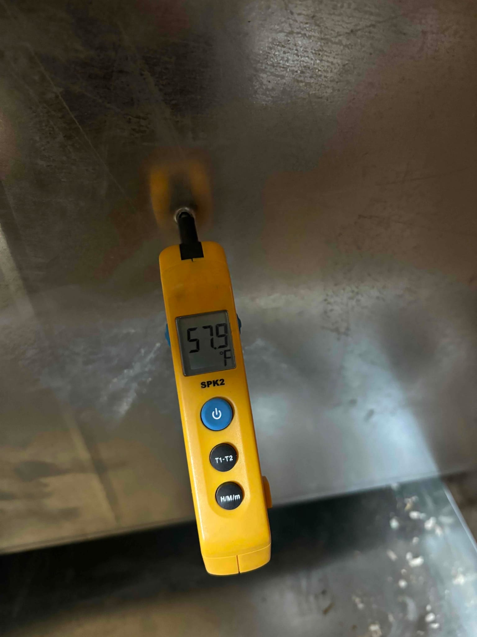 Digital thermometer probe inserted into metal duct reads 57.9°F, documenting supply air temperature leaving the evaporator.