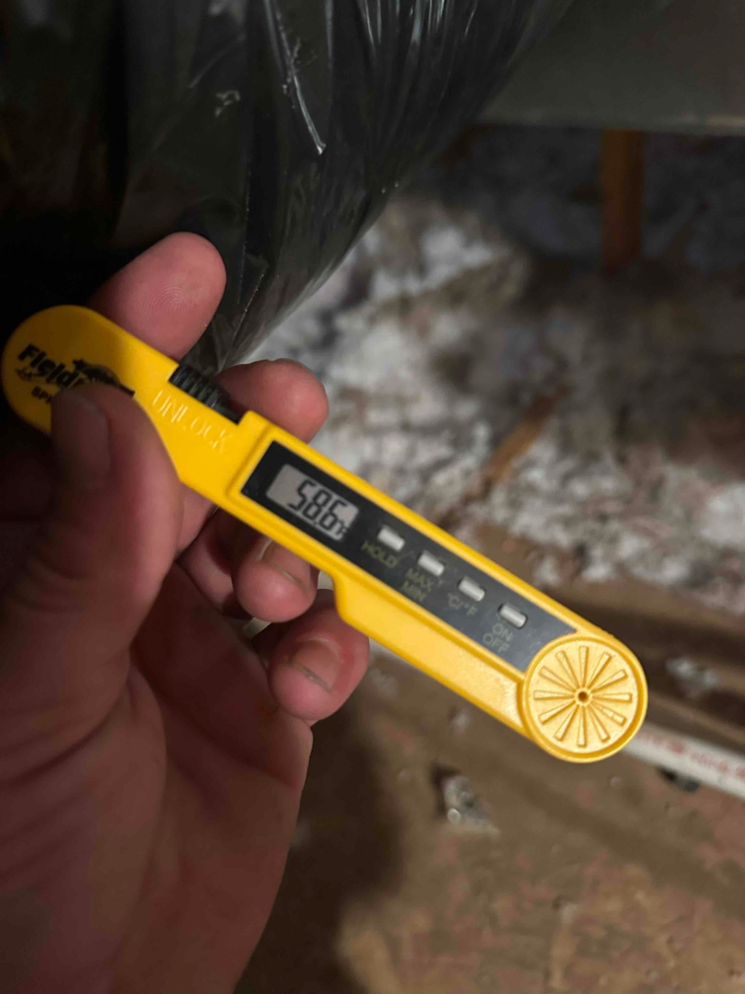 Digital thermometer reads 58.6°F at a duct, documenting supply air temperature during cooling operation.