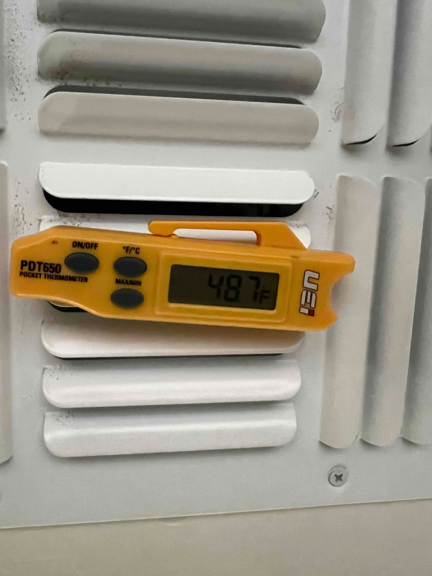 Digital thermometer shows 48.7 °F at a supply register grille during air conditioning operation.