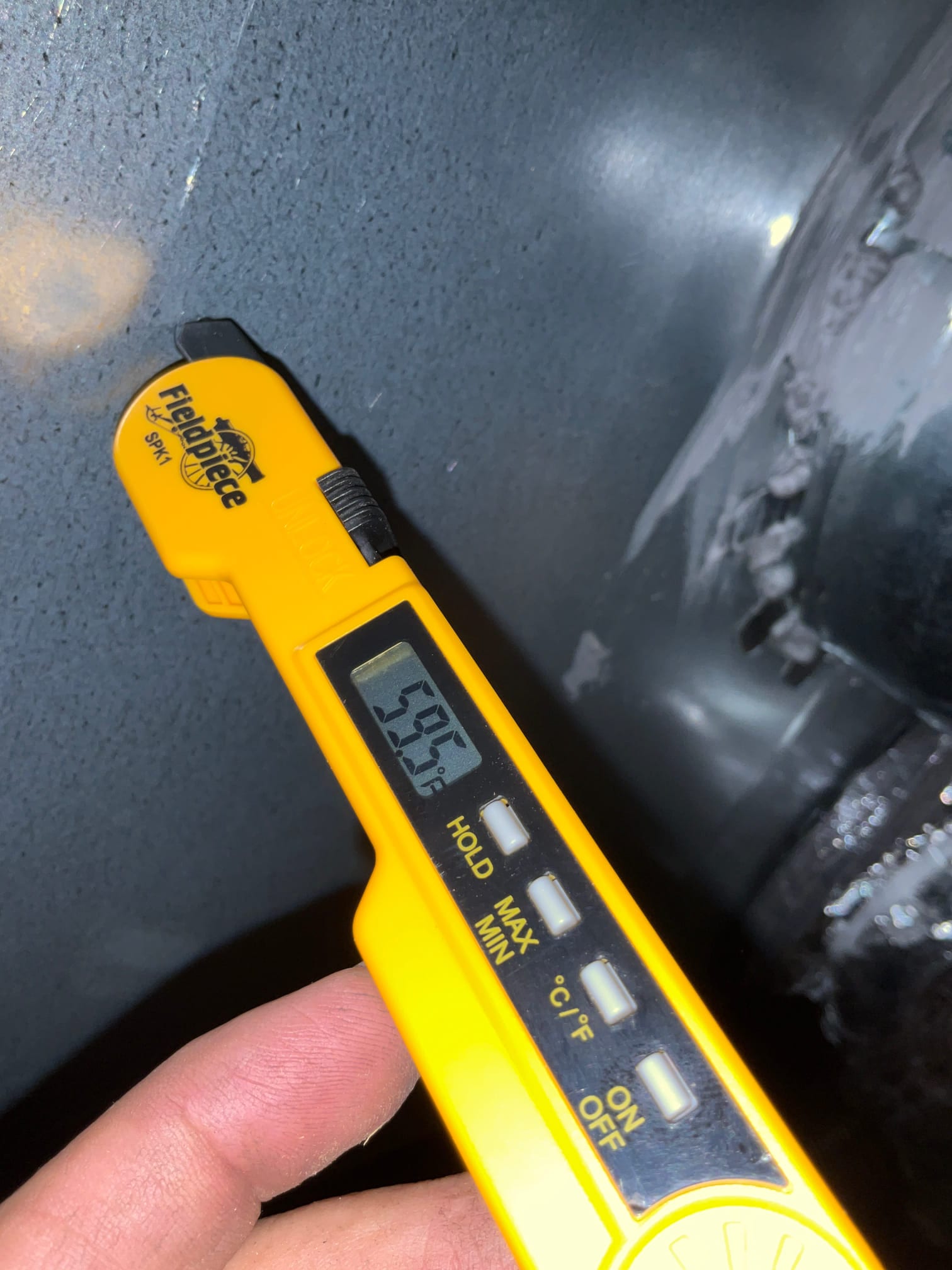 Digital thermometer shows 59.8°F while measuring air temperature at the HVAC duct during commissioning.