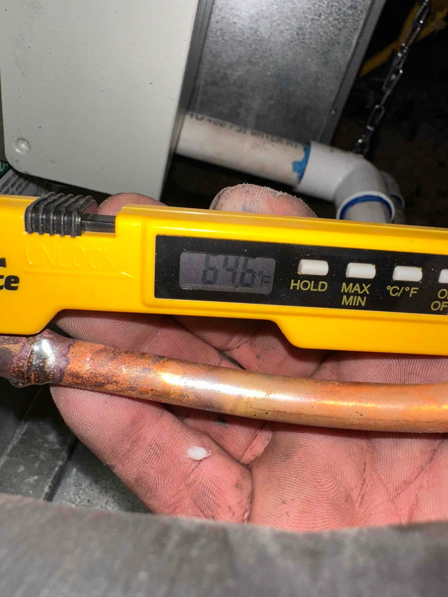 Digital thermometer shows 64.6°F while checking temperature on a copper line near the air handler and condensate drain.