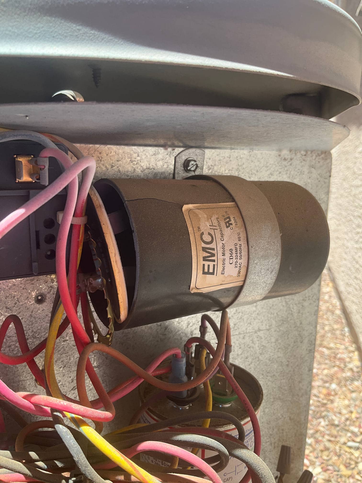 Fan motor housing with label and multiple wires adjacent to a dual-run capacitor and terminal connections inside the condenser cabinet.