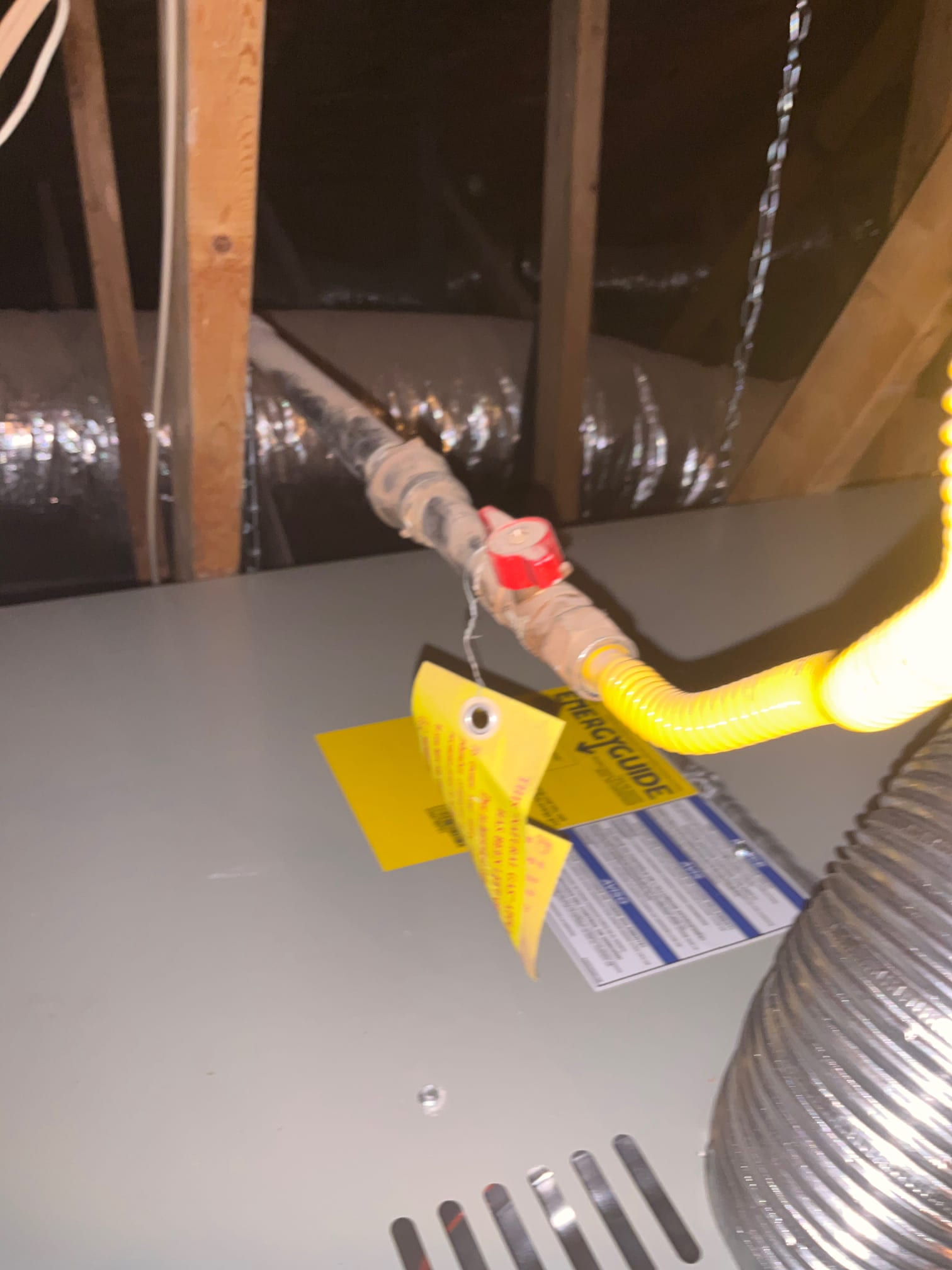 Gas shutoff valve and yellow flexible gas connector installed atop the attic air handler, with ducting visible in the background.