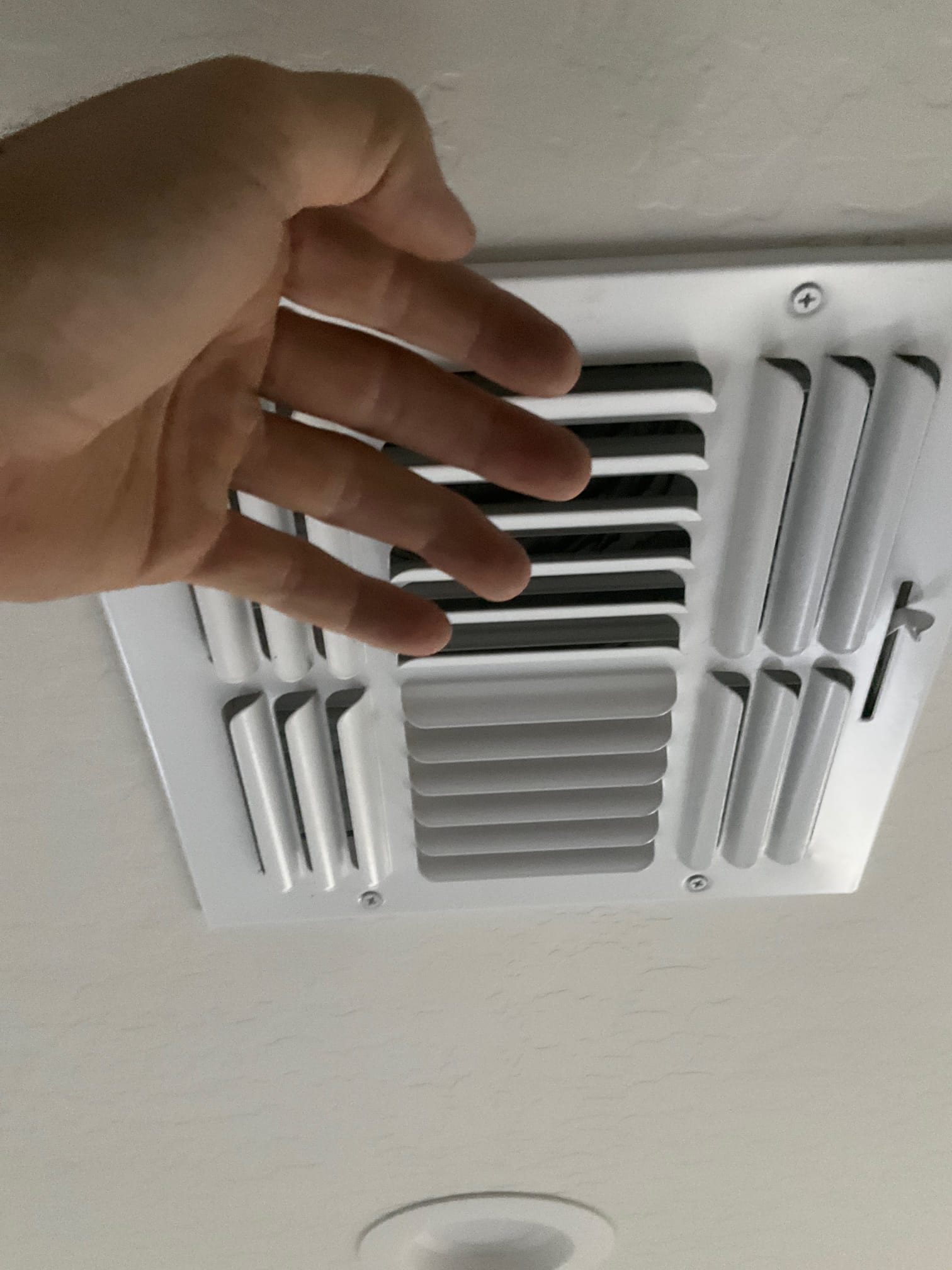 Hand held near a ceiling air supply register with adjustable louvers and center directional vane.