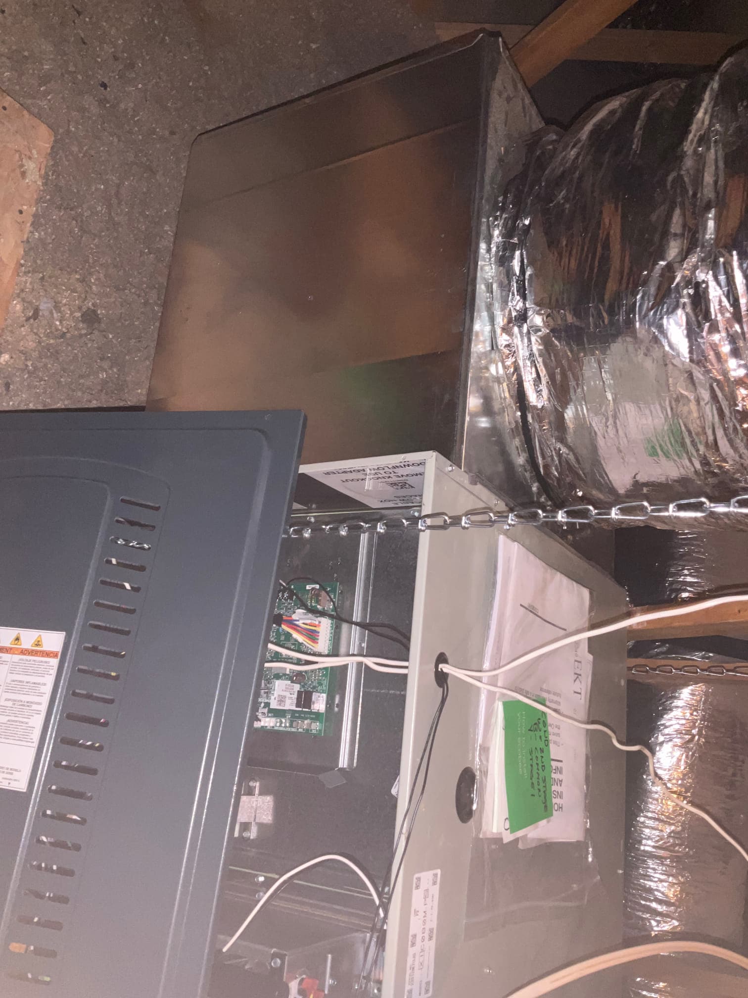 Horizontal attic air handler hung with chains, connected to insulated flexible duct and metal transition, control board visible with wiring.