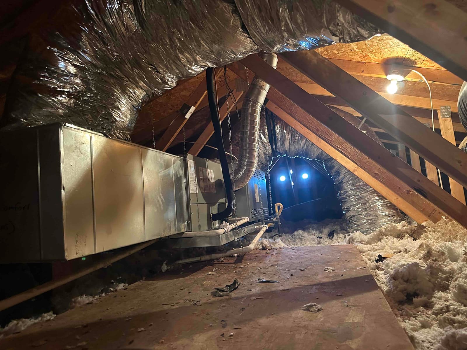 Horizontal attic air handler with insulated ductwork, hanging supports, and condensate drain lines installed along the attic walkway.