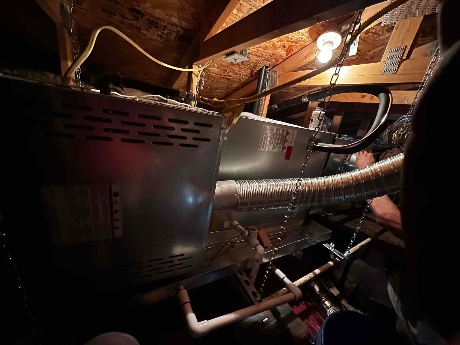 Horizontal attic air handler suspended with chains, connected to metal duct, condensate piping, and flexible gas line during installation.
