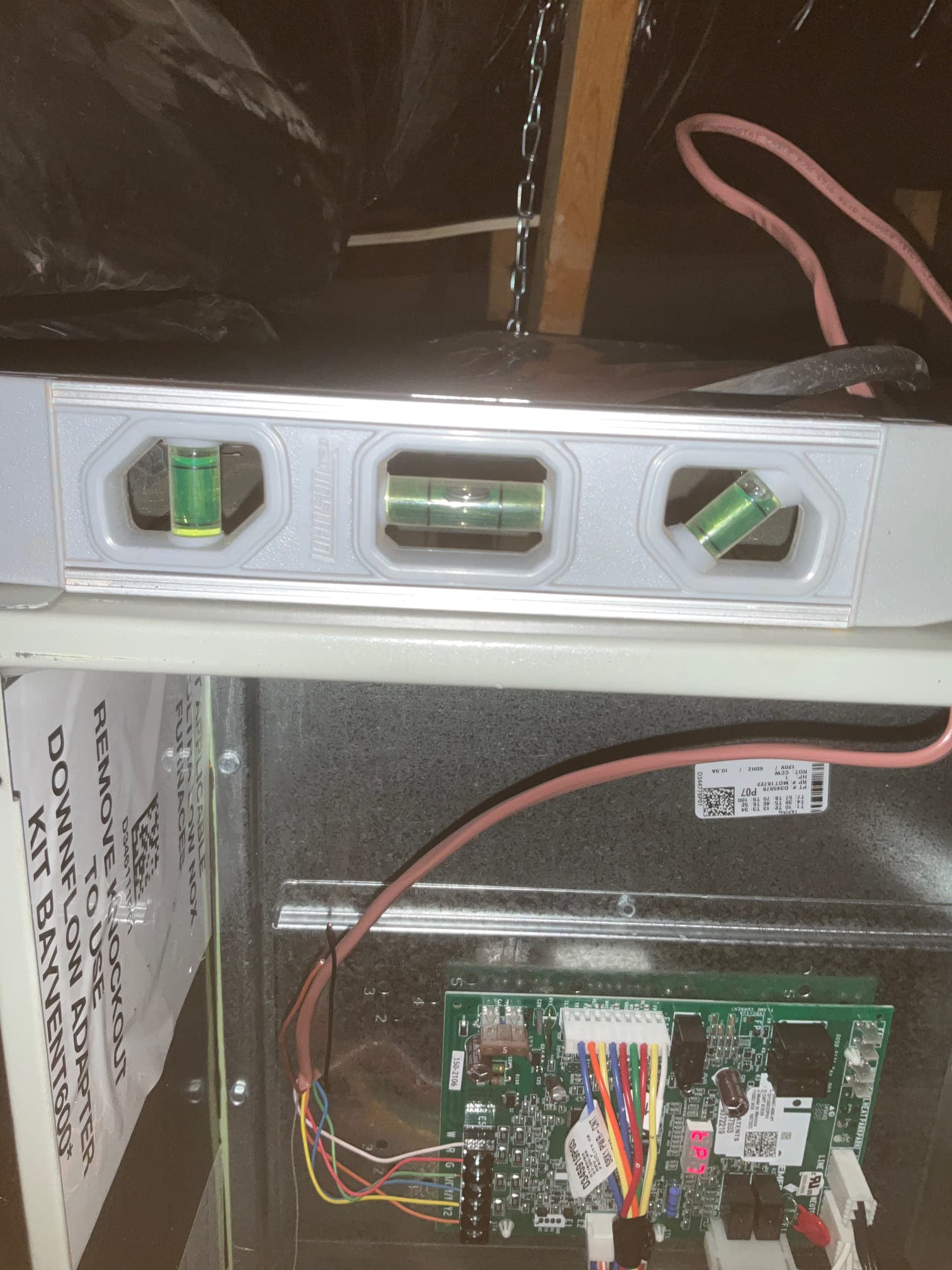 Level placed on furnace cabinet while control board wiring and harness connections are visible inside the blower compartment.