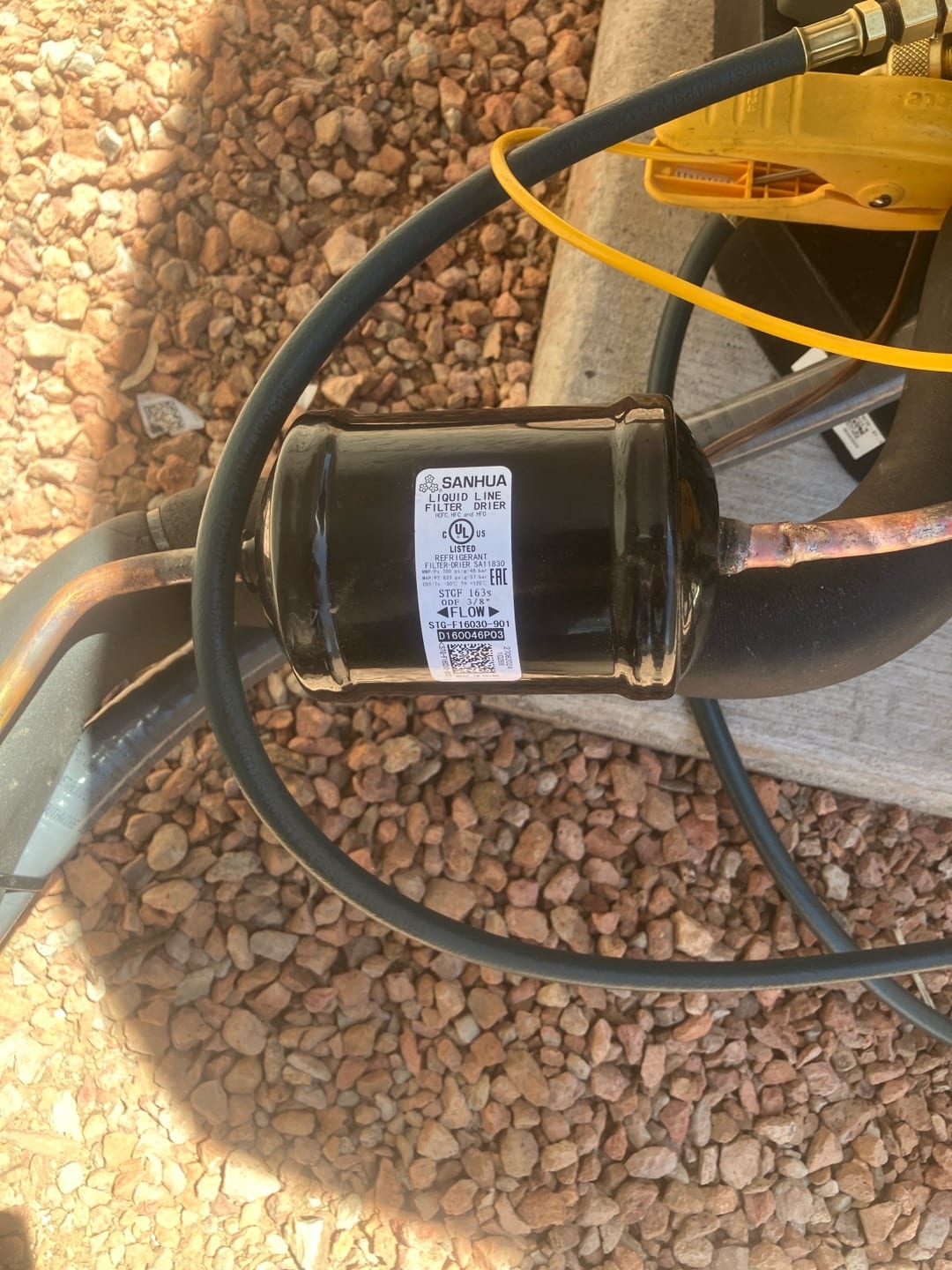 Liquid line filter drier brazed into the refrigerant line near the outdoor unit, with hoses and tools visible around the installation.