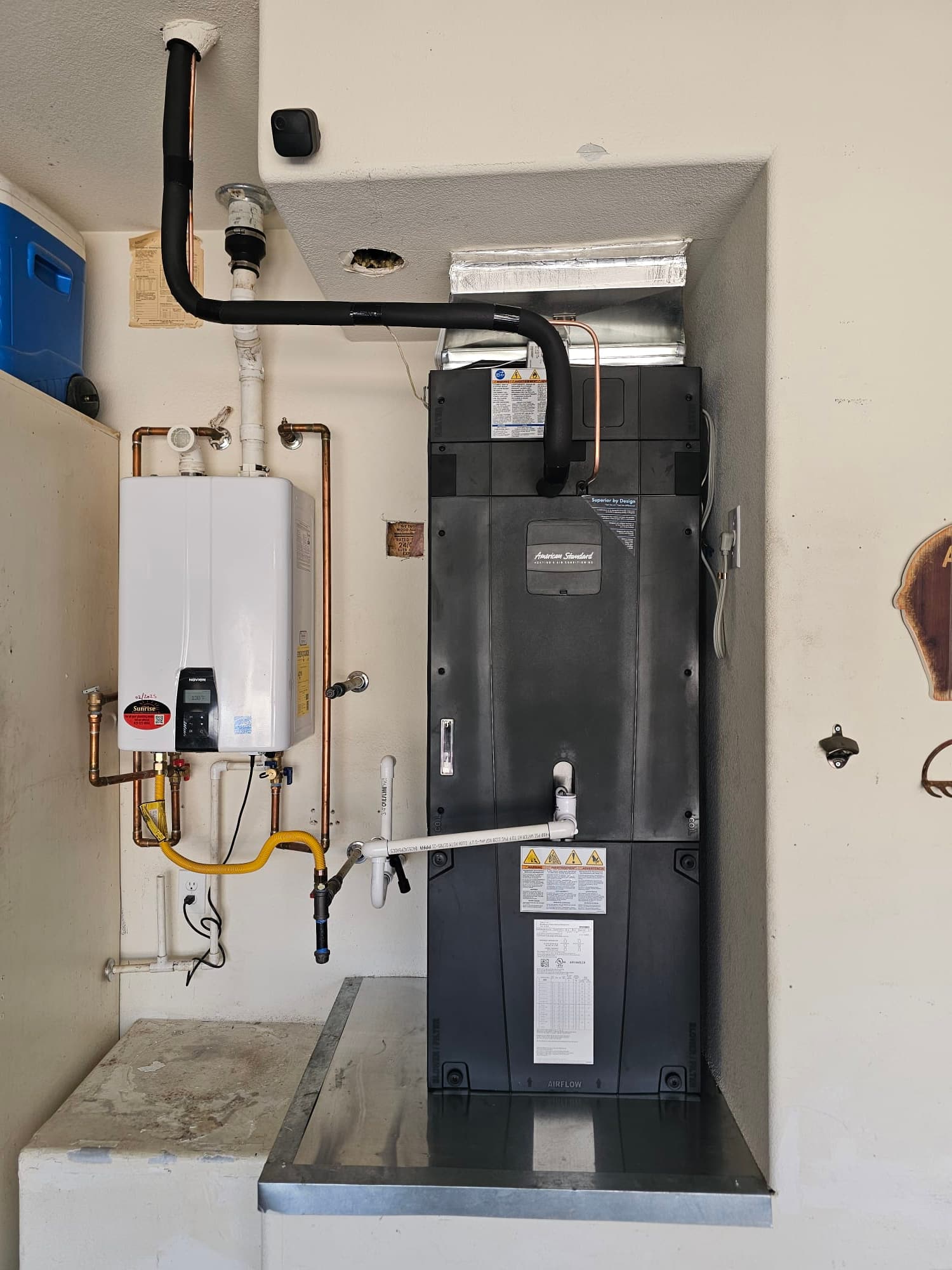 New air handler installed on a drain pan with insulated refrigerant lines, condensate plumbing, and adjacent tankless water heater piping.
