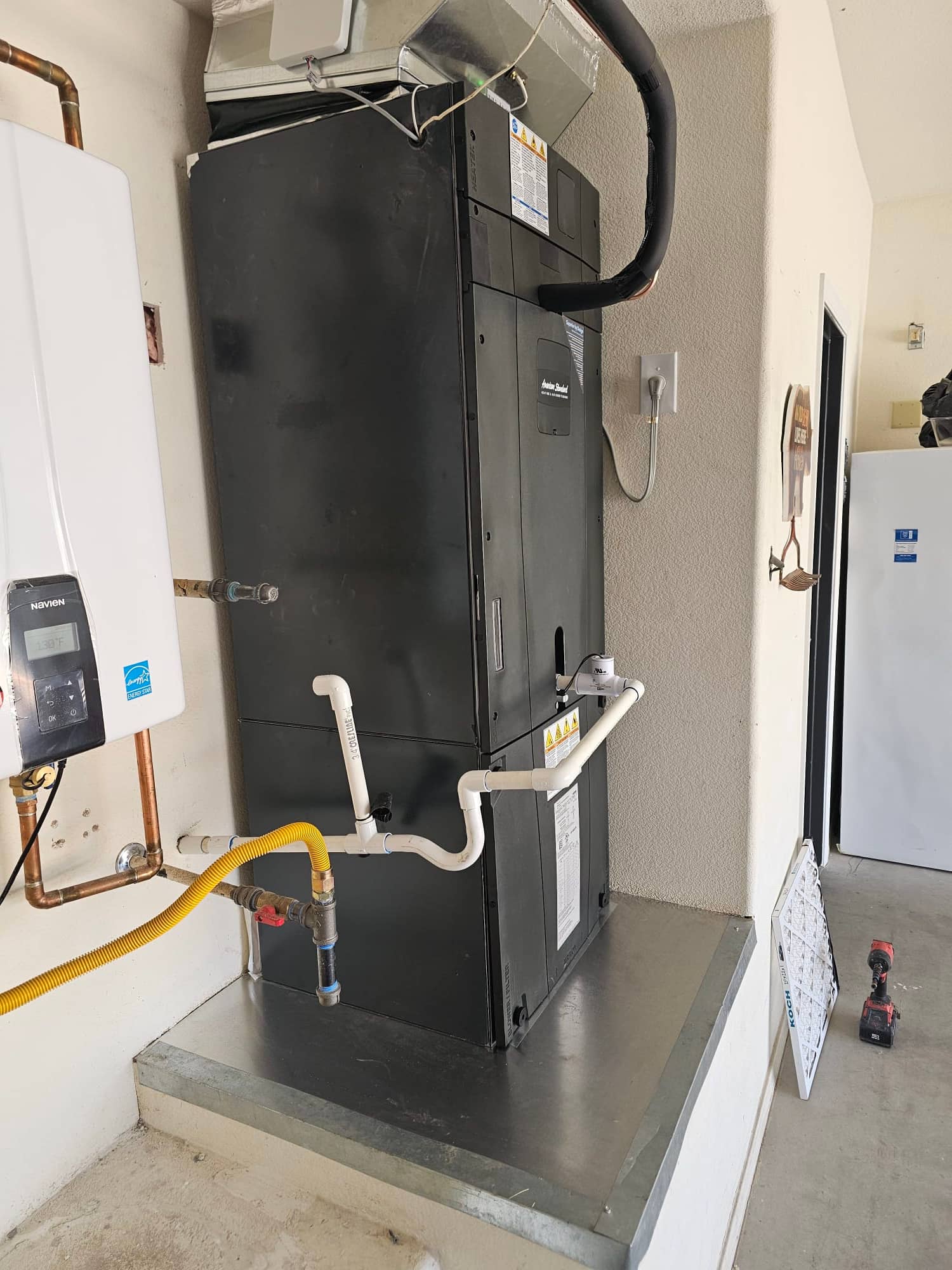 New air handler installed on a platform with insulated refrigerant line, condensate drain piping, and connected duct transition above.
