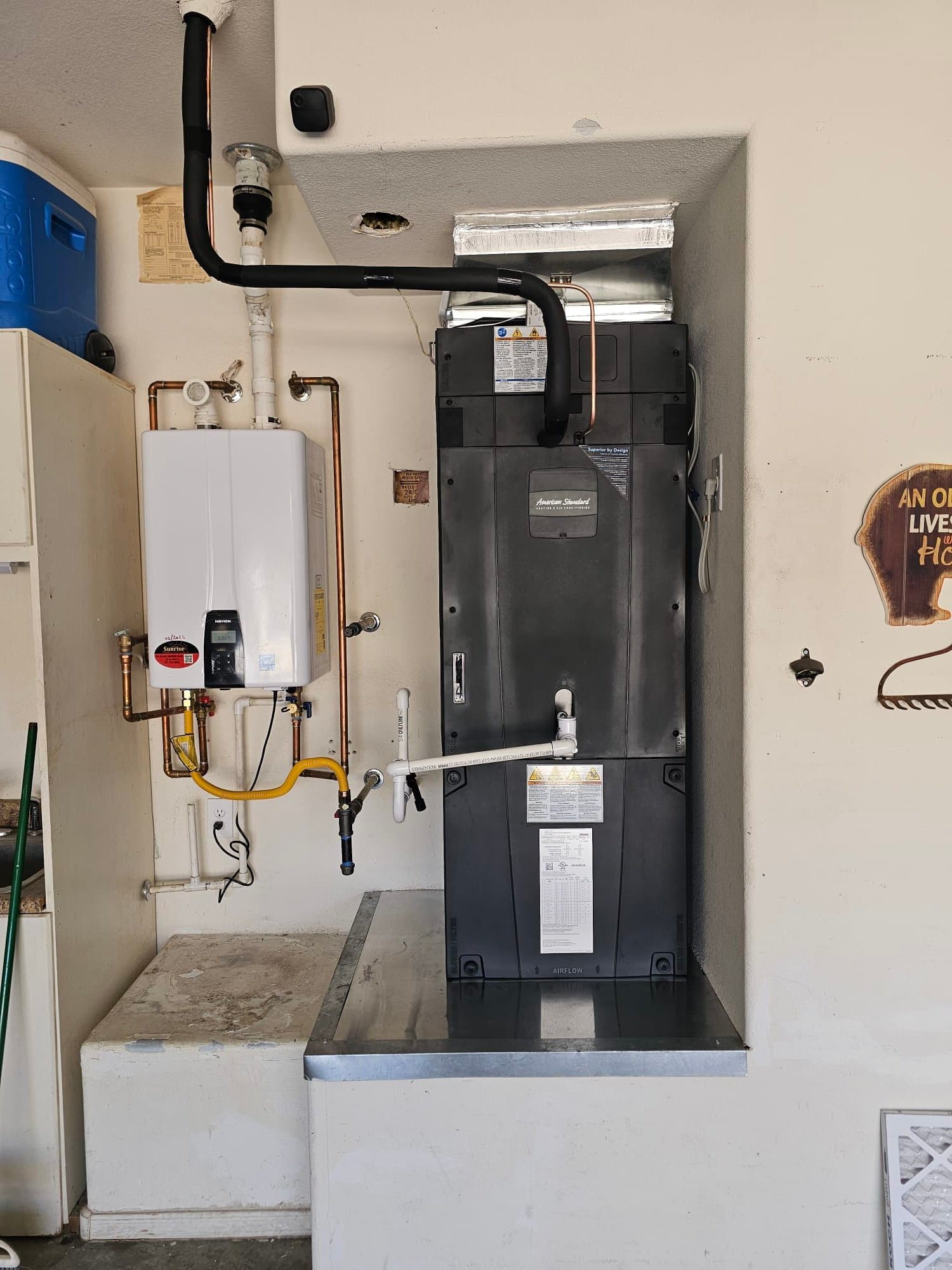 New air handler set on a metal platform with insulated refrigerant lines, condensate drain, and connected duct transition in a garage space.