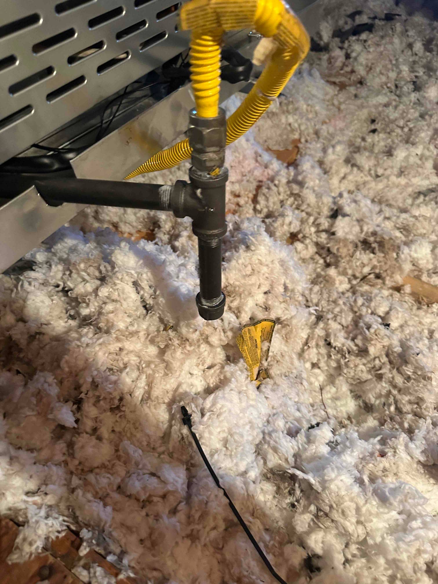 New gas flex connector and black iron drip leg installed at the furnace in the attic insulation.