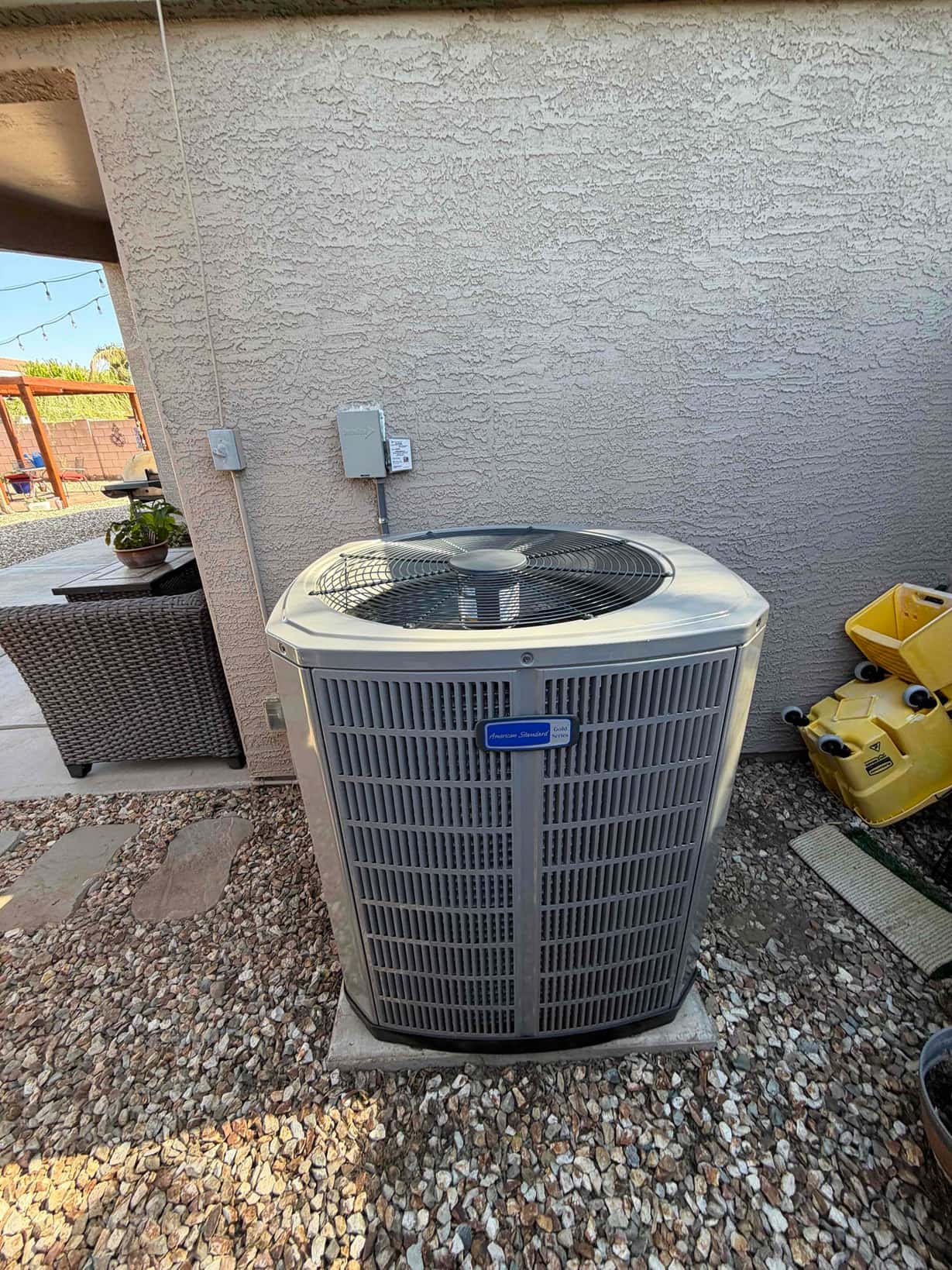 New heat pump condenser set on a level pad beside the house with outdoor disconnect mounted and line set penetration sealed.