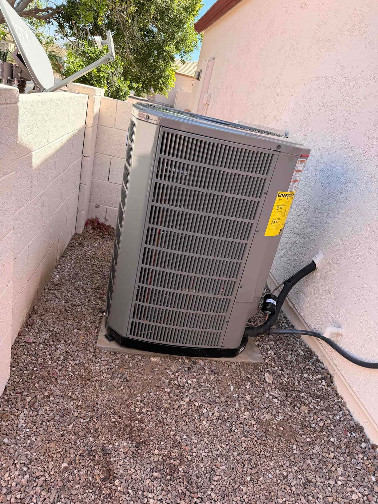 New heat pump condenser set on a level pad with insulated refrigerant lines and electrical whip routed to the wall.