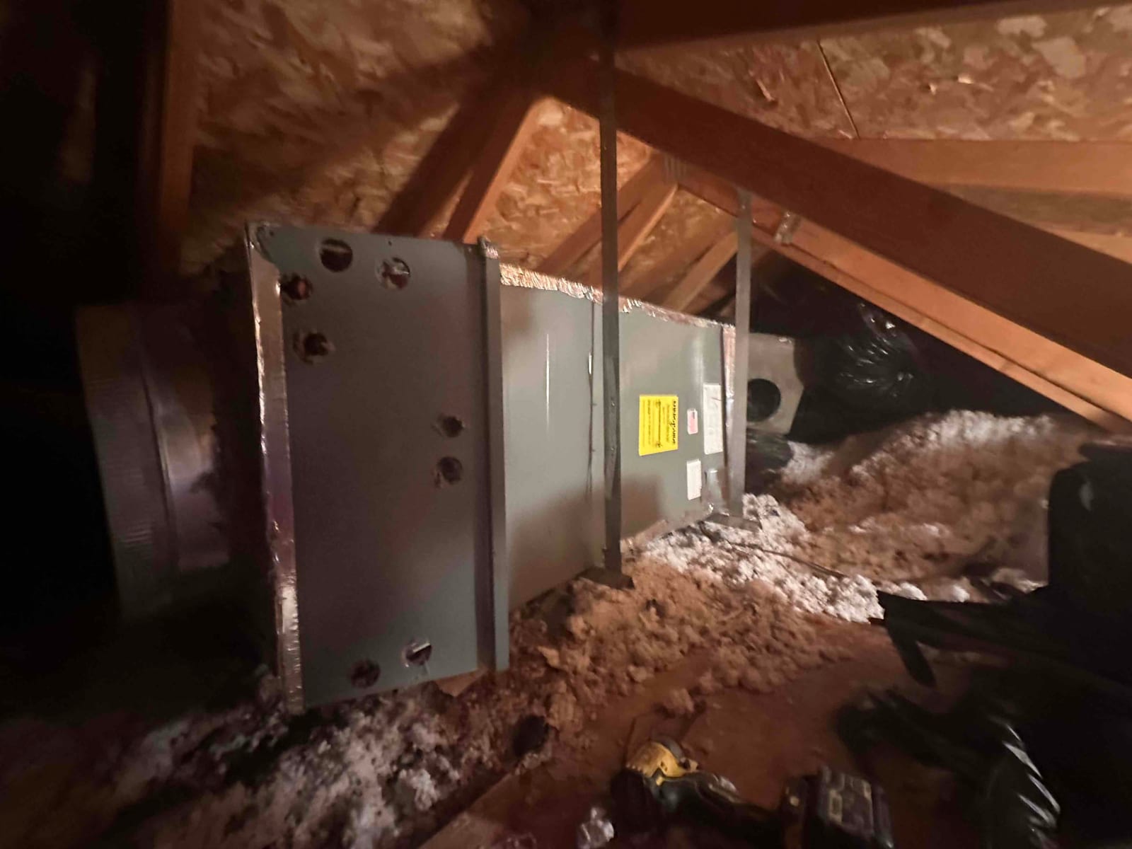 New horizontal air handler suspended in the attic with duct connections and surrounding blown-in insulation visible.