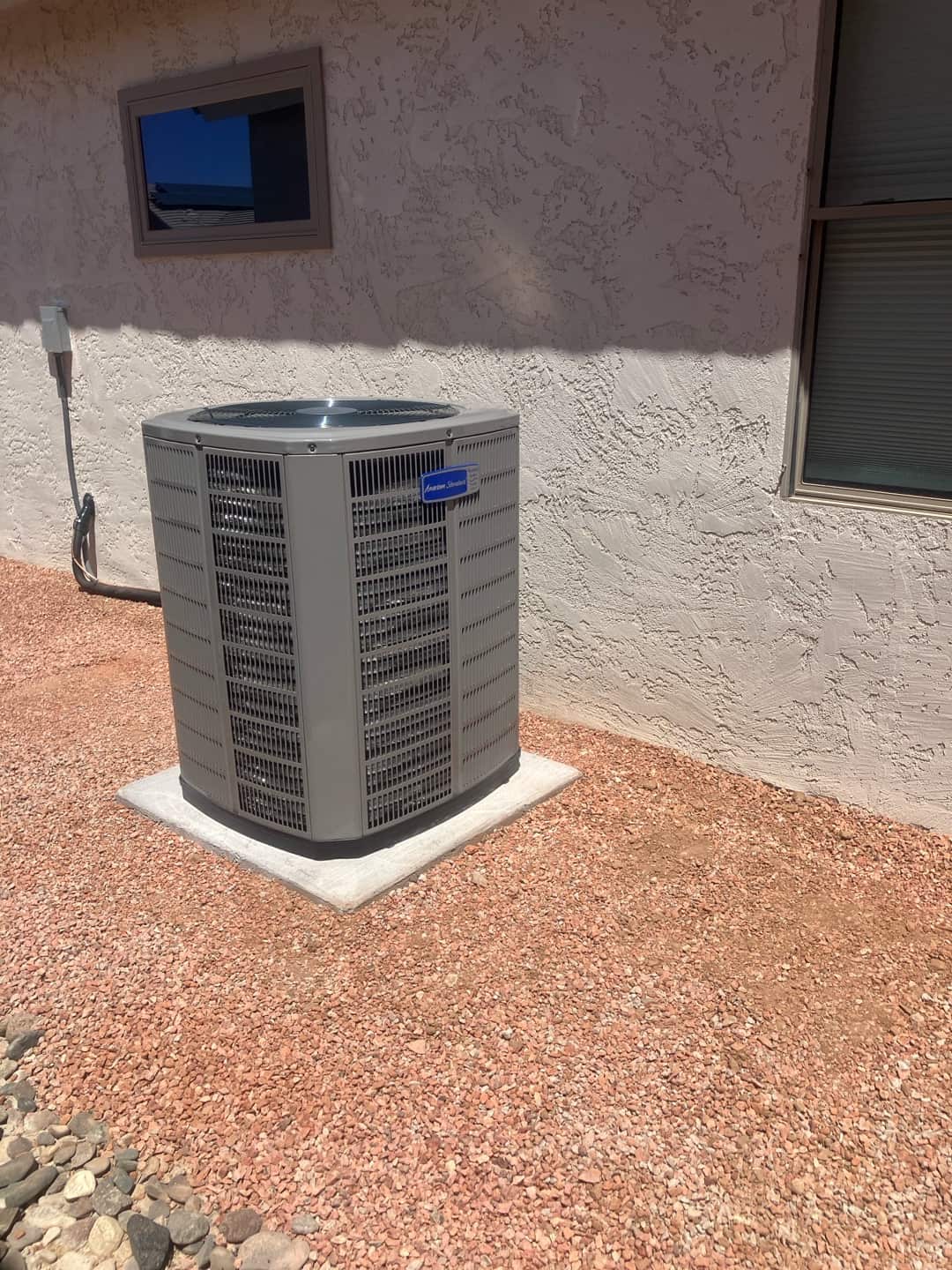 New outdoor condenser installed on a level pad with electrical whip and disconnect mounted on the wall nearby.