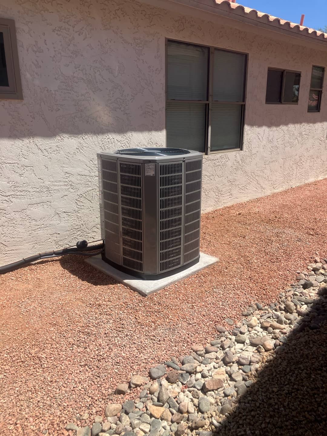 New outdoor condenser set on a level concrete pad with insulated line set routed along the wall in a clean yard.