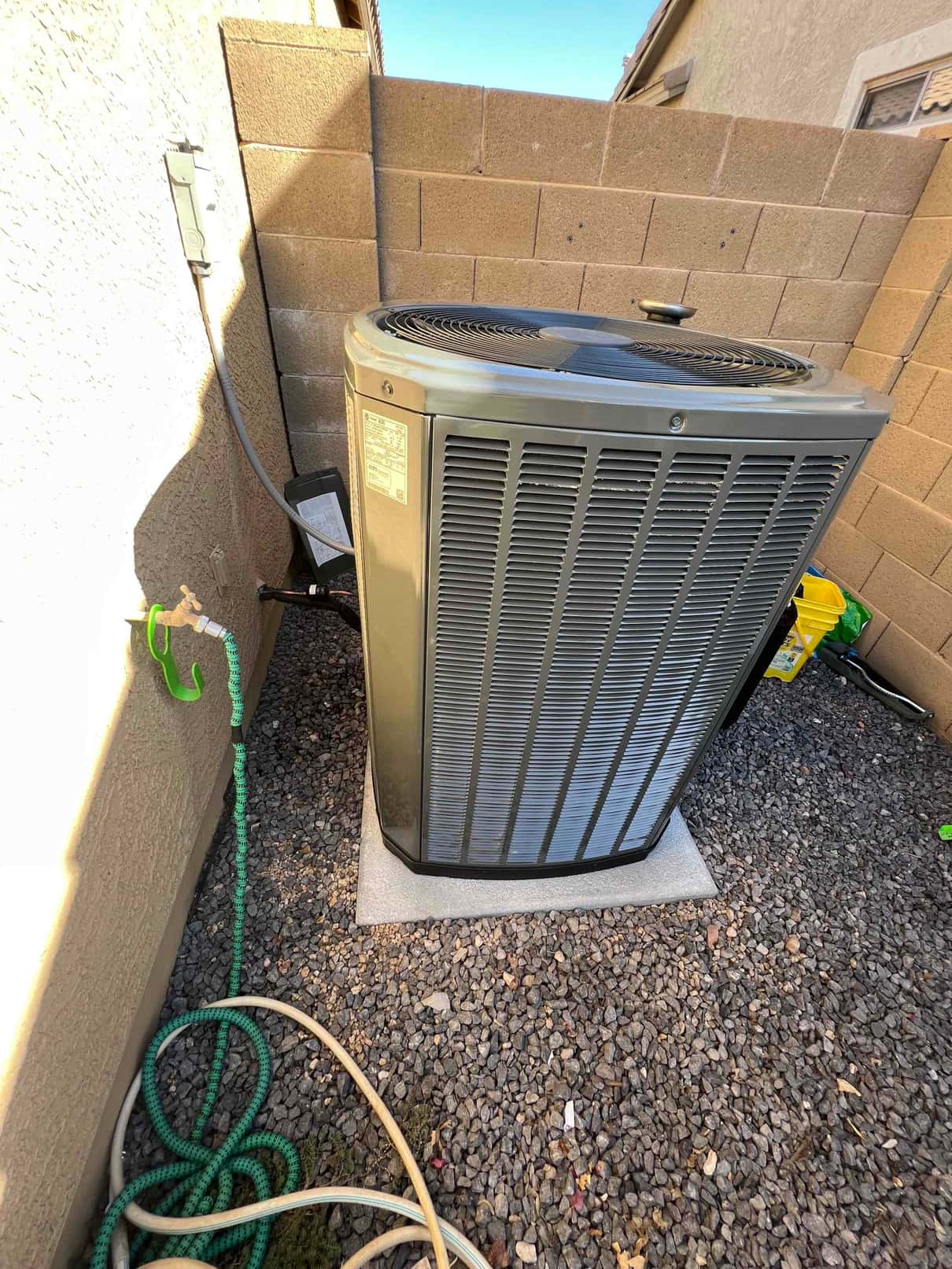 New outdoor condenser set on a level pad with connected electrical disconnect and insulated refrigerant lines in a side yard.