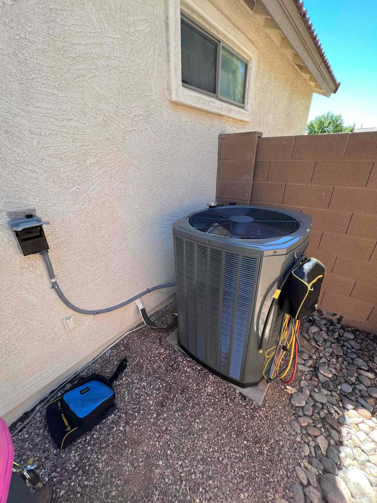 New outdoor condenser set on a level pad with insulated line set, disconnect, and service gauges hanging on the unit.