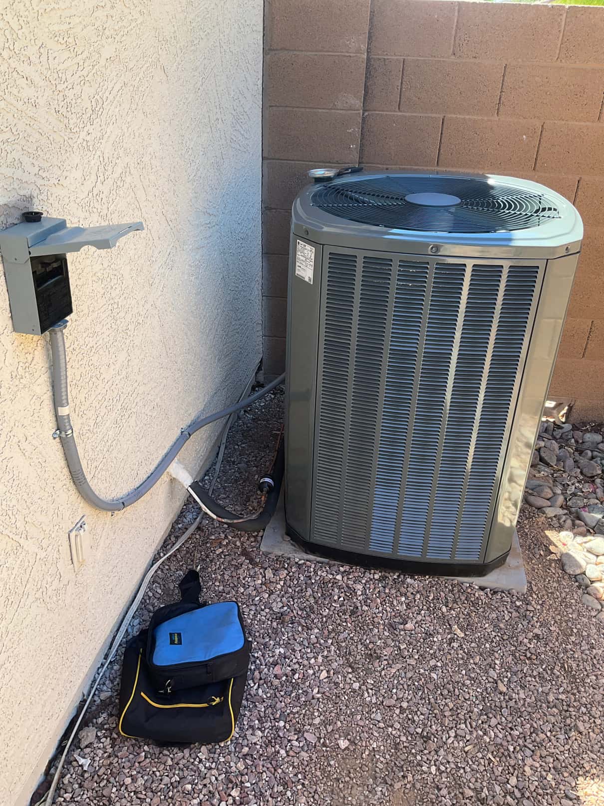 New outdoor condenser set on a level pad with insulated line set, sealed wall penetration, and mounted electrical disconnect.