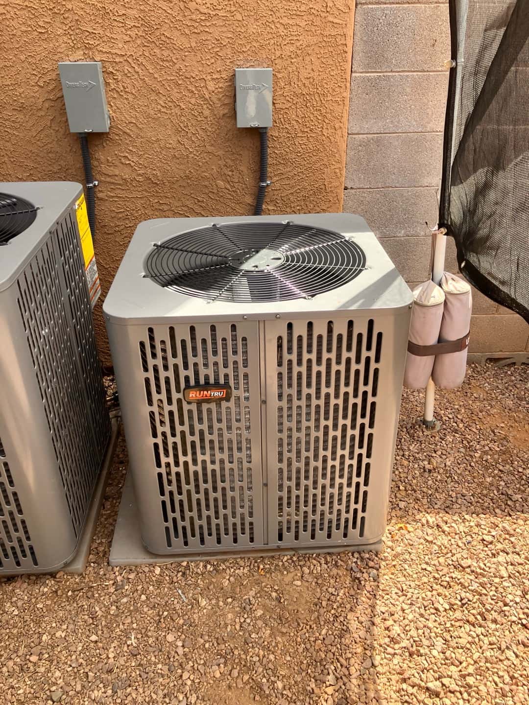 New outdoor condenser set on a level pad with insulated line set and weatherproof disconnect mounted on the wall.