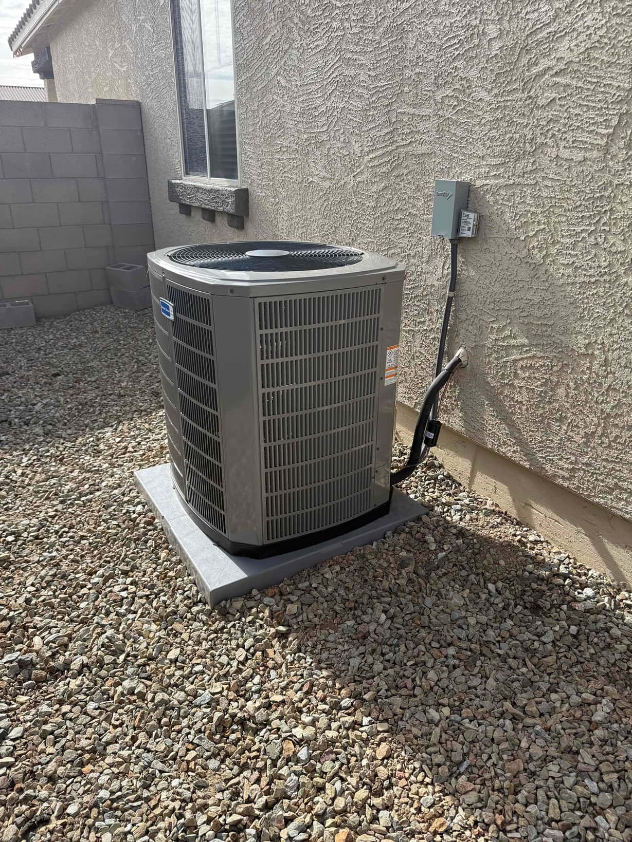 New outdoor condenser set on a level pad with insulated refrigerant lines and a mounted electrical disconnect.