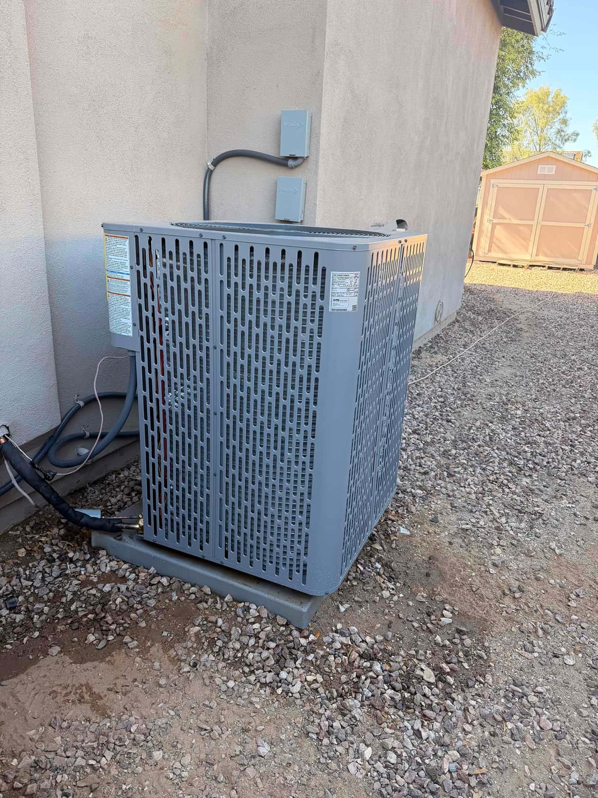 New outdoor condenser set on a level pad with insulated refrigerant lines and weatherproof electrical disconnects mounted on the wall.