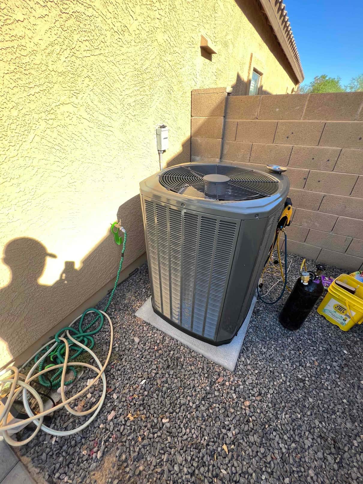 New outdoor condenser set on a level pad with insulated refrigerant lines connected and service disconnect mounted on the wall.