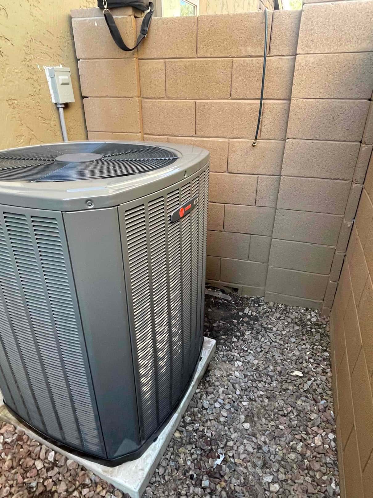 New outdoor condenser set on a level pad with nearby electrical disconnect, installed in a gravel side yard alcove.