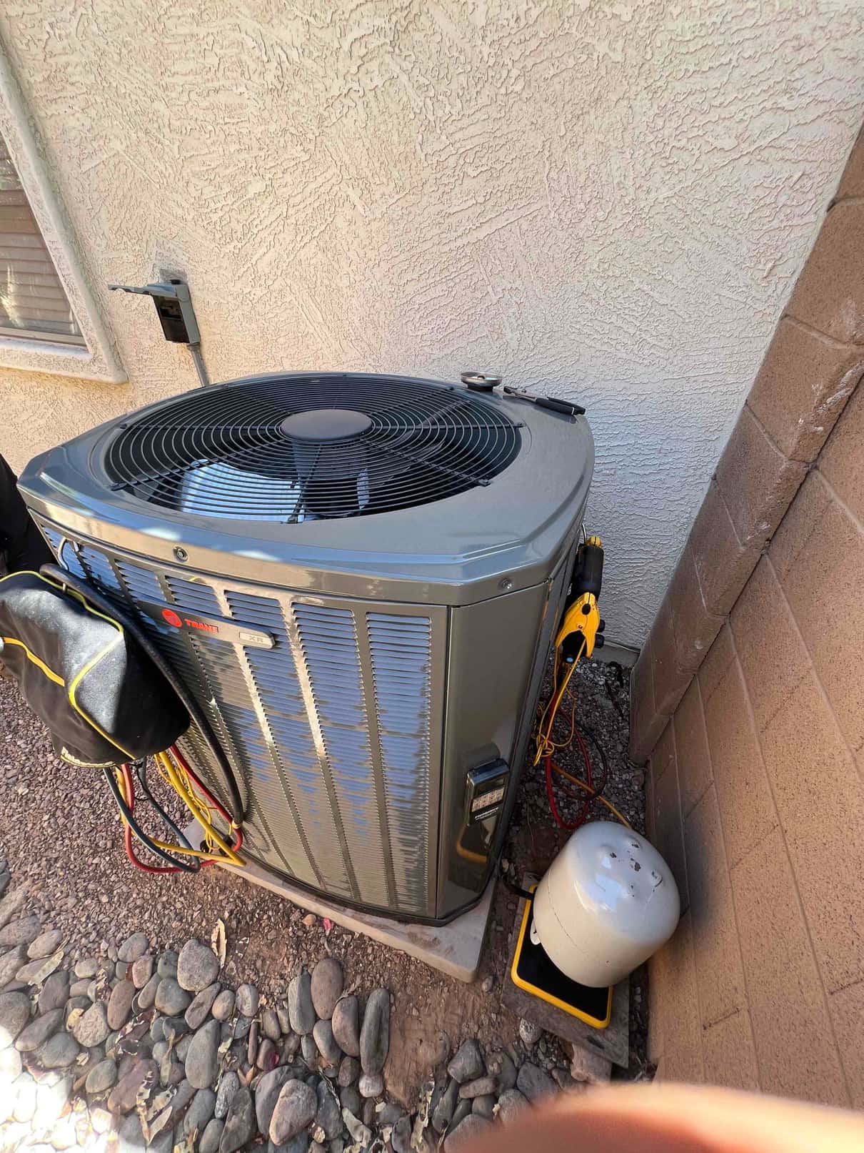 New outdoor condenser set on a level pad with service disconnect and hoses connected for commissioning at the installation site.