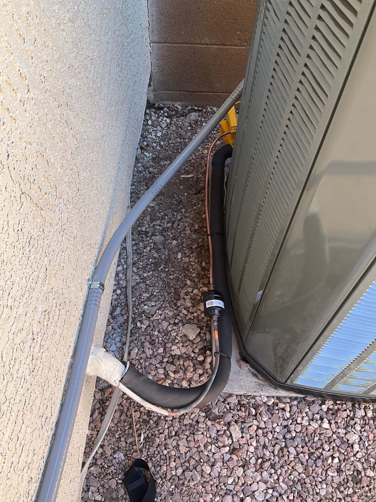New outdoor condenser set on pad with insulated suction line, liquid line filter-drier, and electrical conduit neatly routed along the wall.