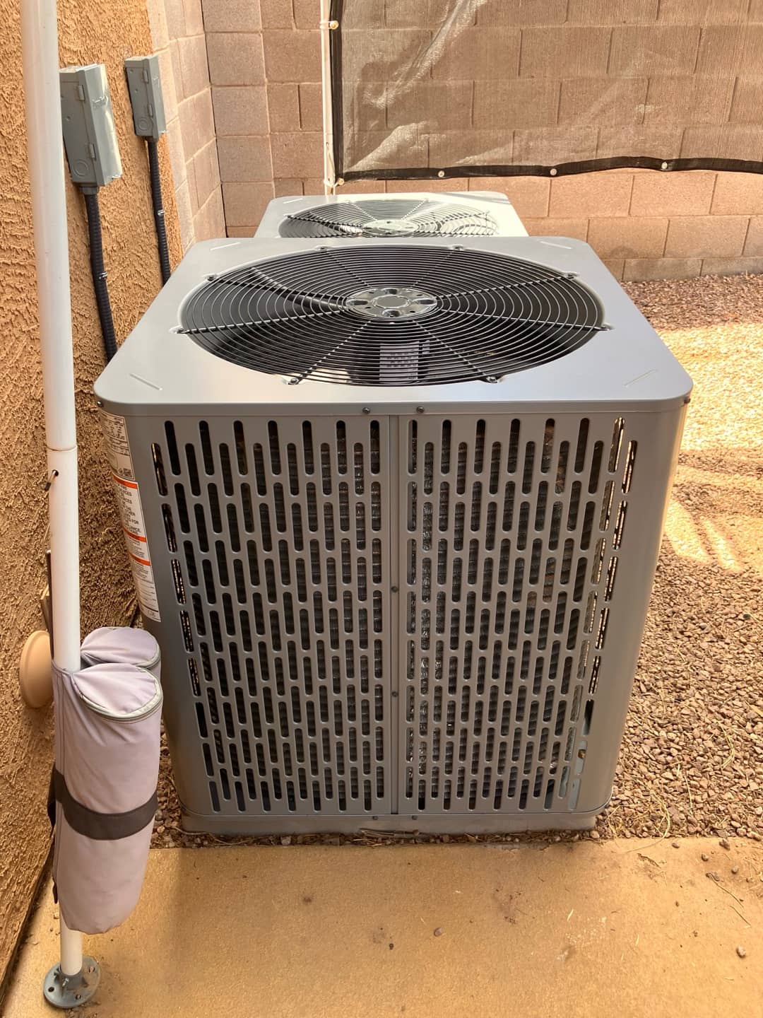 Two new outdoor condensers set on level pads with electrical disconnects and insulated refrigerant lines routed along the wall.