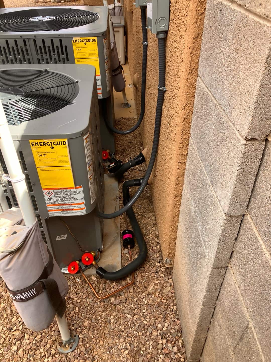 Two new outdoor condensers set on pads with insulated refrigerant lines, filter drier, and mounted electrical disconnects along the wall.