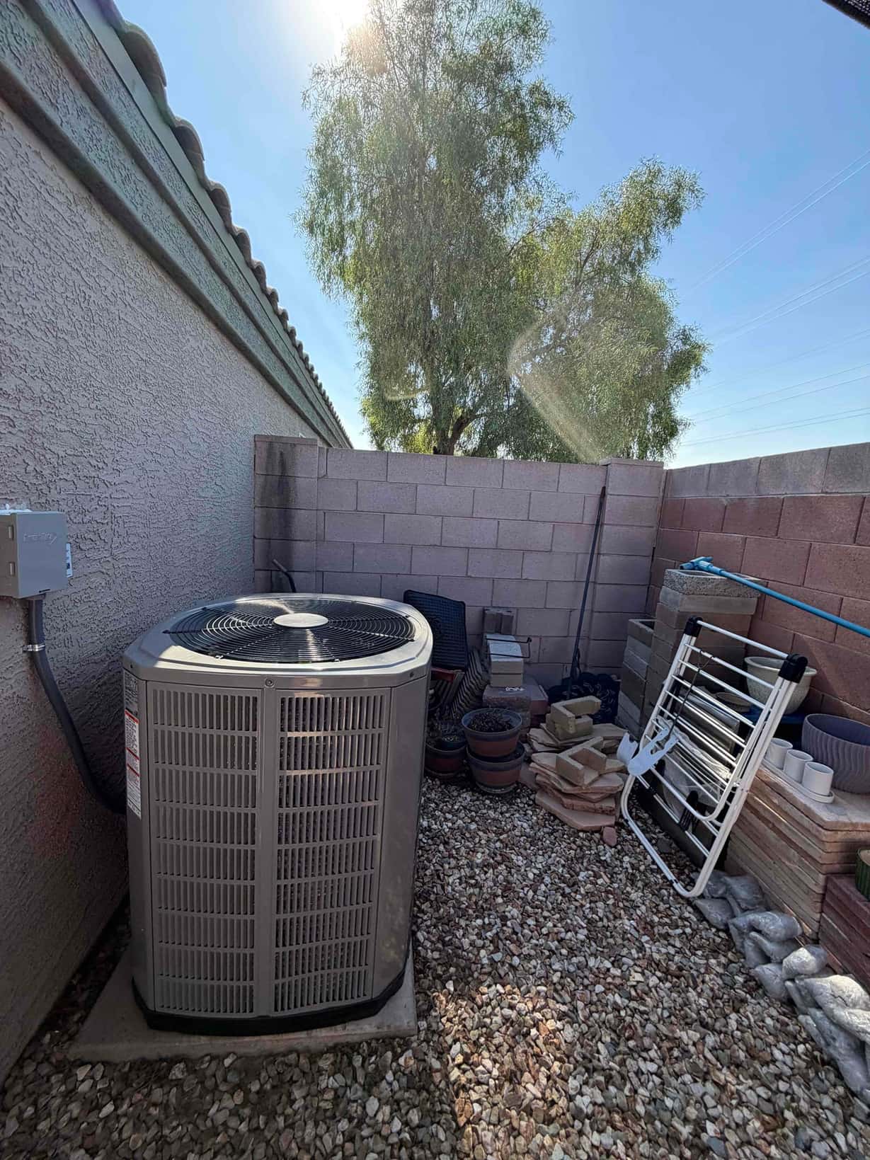 New outdoor heat pump condenser set on a level concrete pad with electrical disconnect mounted on the wall nearby.
