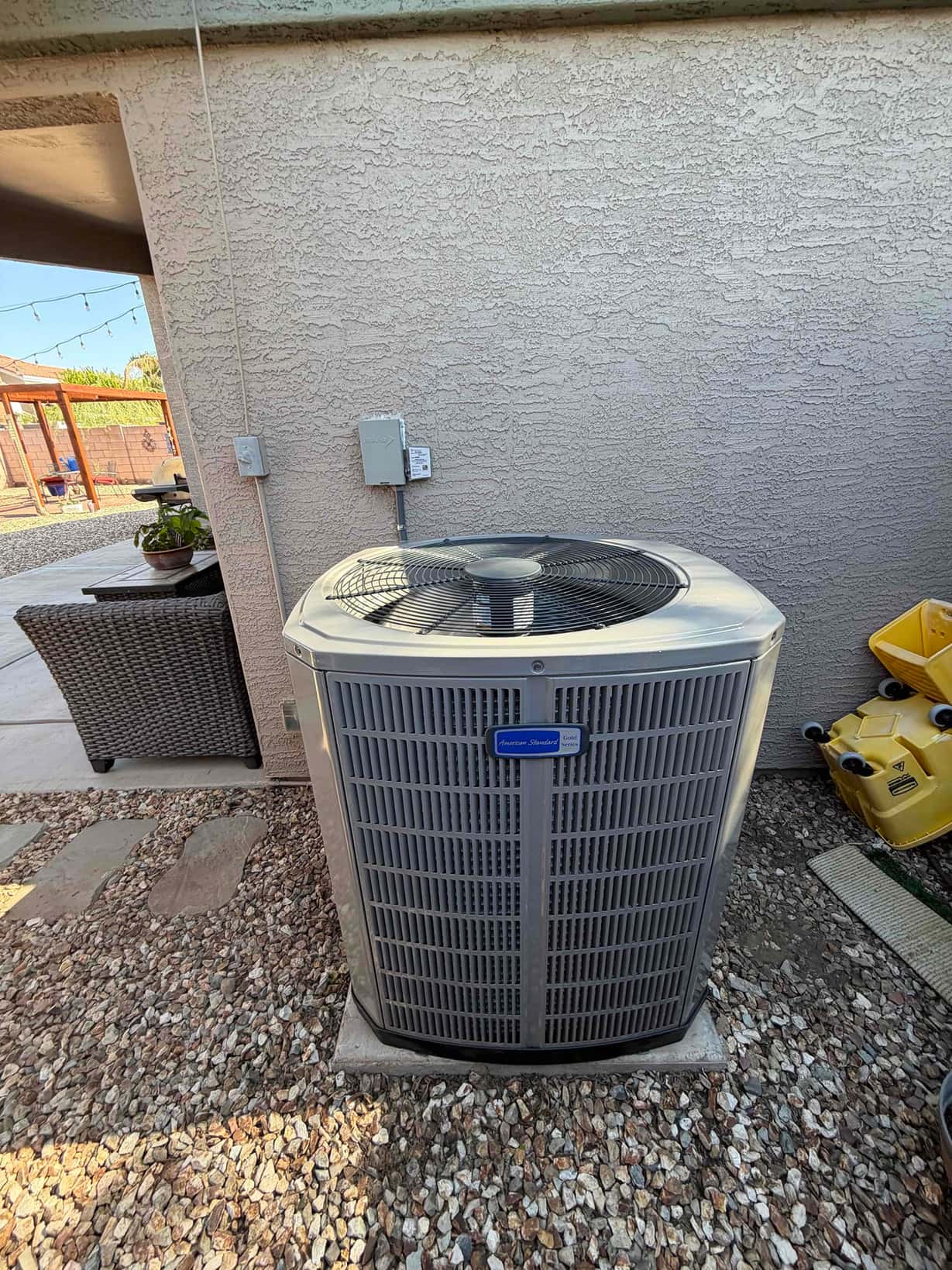 New outdoor heat pump condenser set on a level pad with adjacent disconnect and sealed wall penetration.