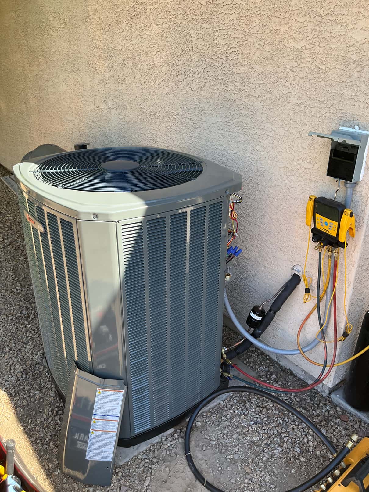 New outdoor heat pump condenser set on a level pad with line set, filter drier, and service gauges connected at the wall.