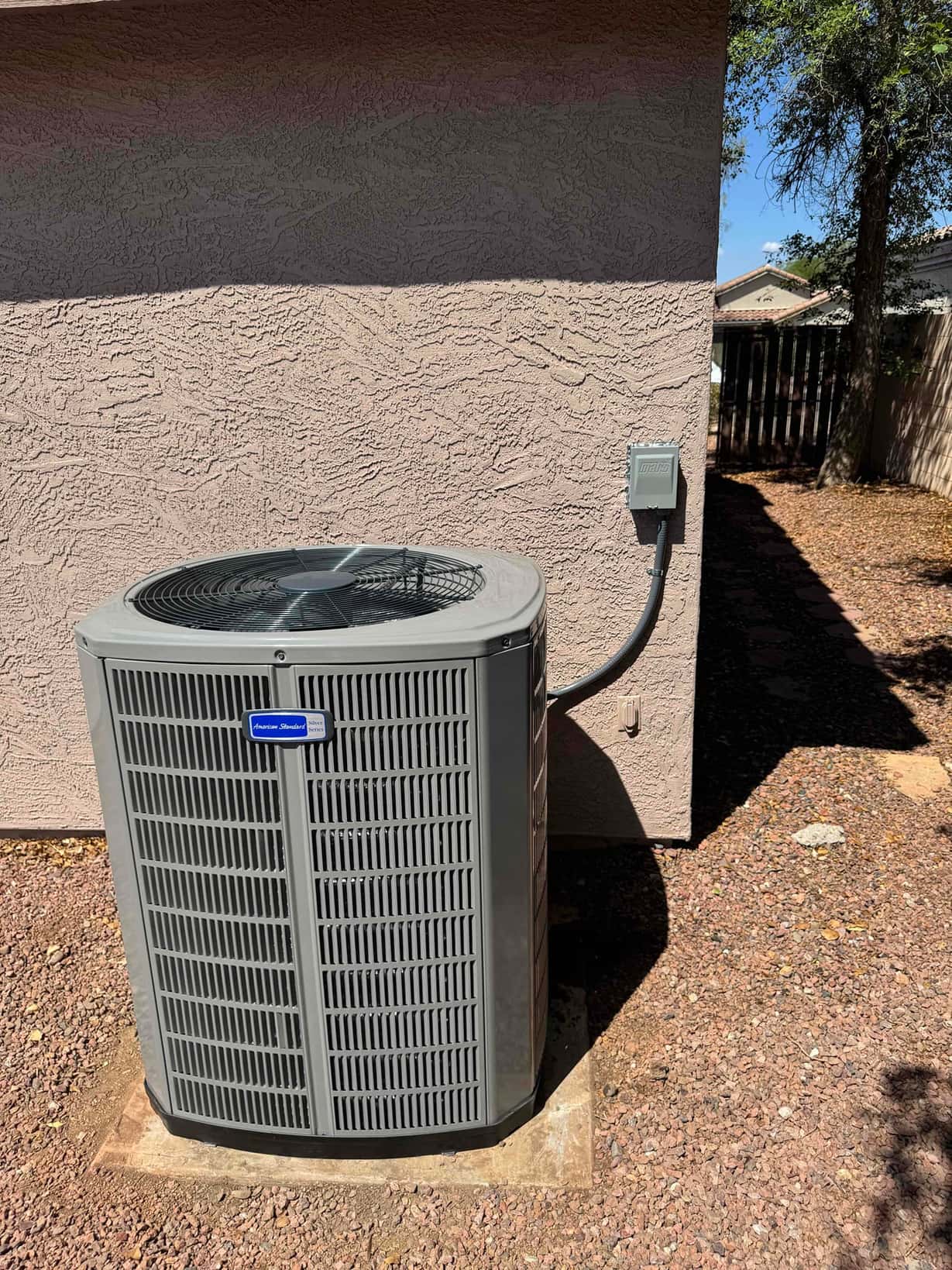 New outdoor heat pump condenser set on a level pad with sealed electrical disconnect and conduit mounted to the wall.