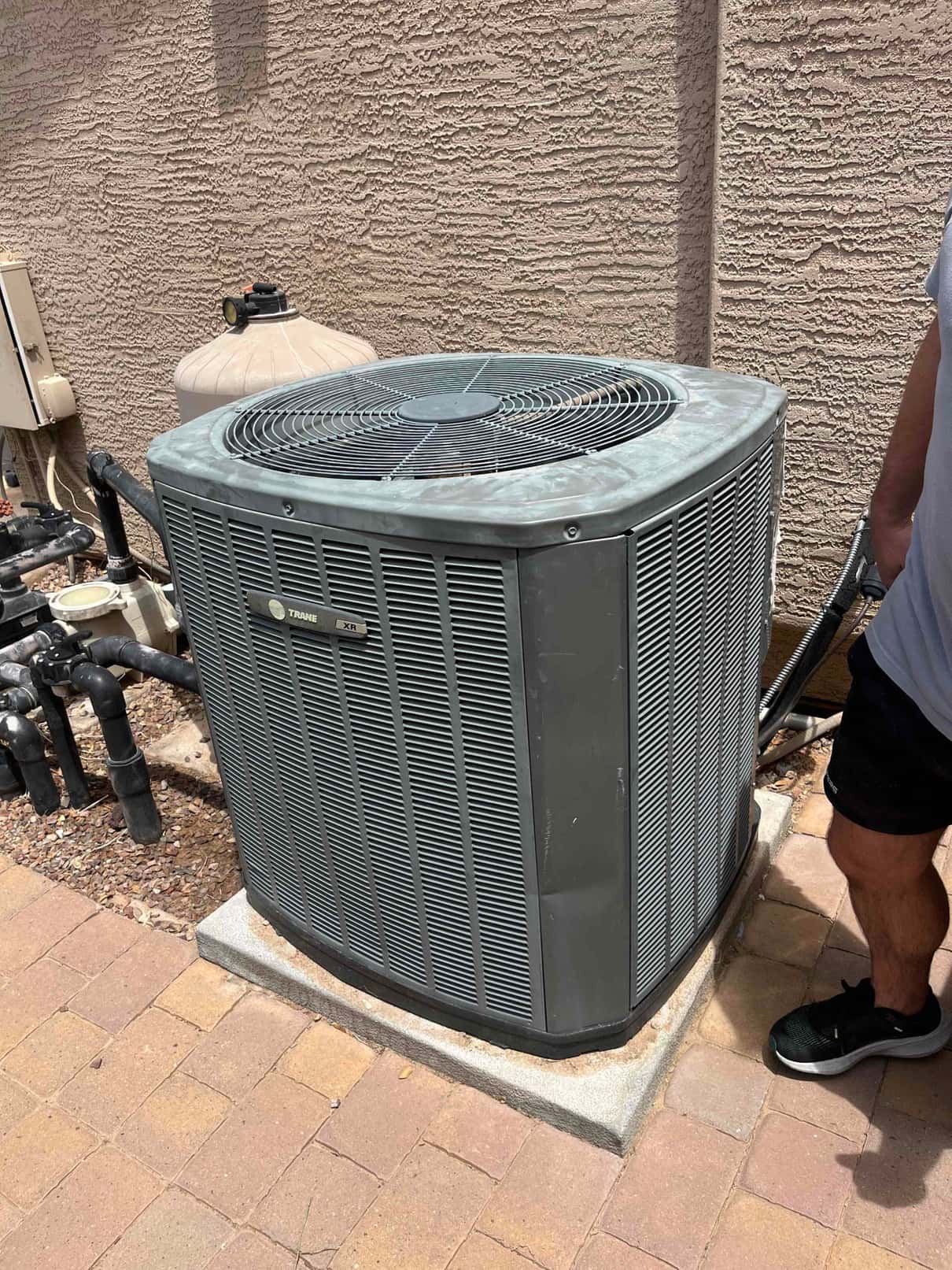 Outdoor air conditioning condenser unit on a pad with refrigerant lines and electrical conduit connected at the side.