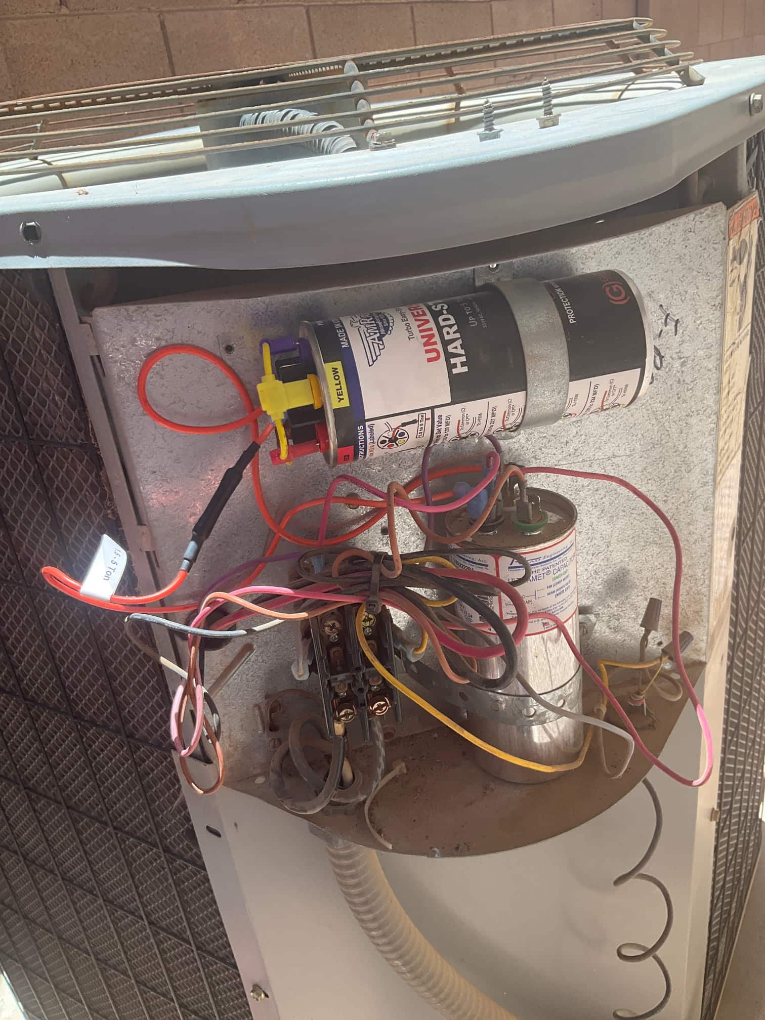 Outdoor condenser control compartment showing dual-run capacitor, contactor terminals, and a hard start kit with connected wiring.