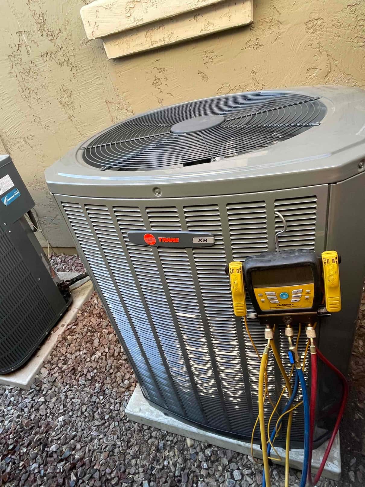 Outdoor condenser set on a level pad with digital manifold gauge connected to service ports using yellow, blue, and red hoses.
