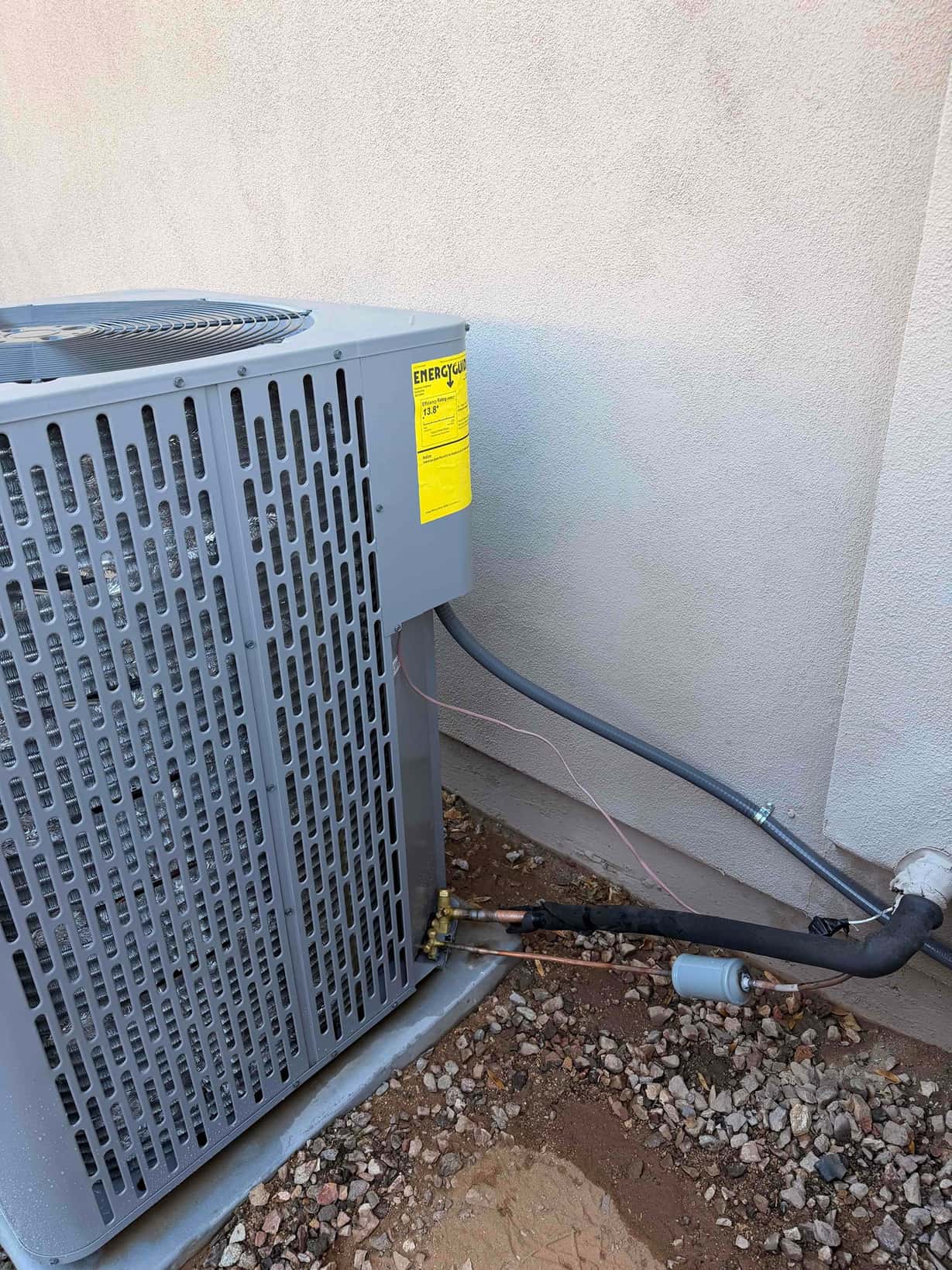 Outdoor condenser set on a level pad with insulated refrigerant line set, filter-drier, and sealed wall penetration.
