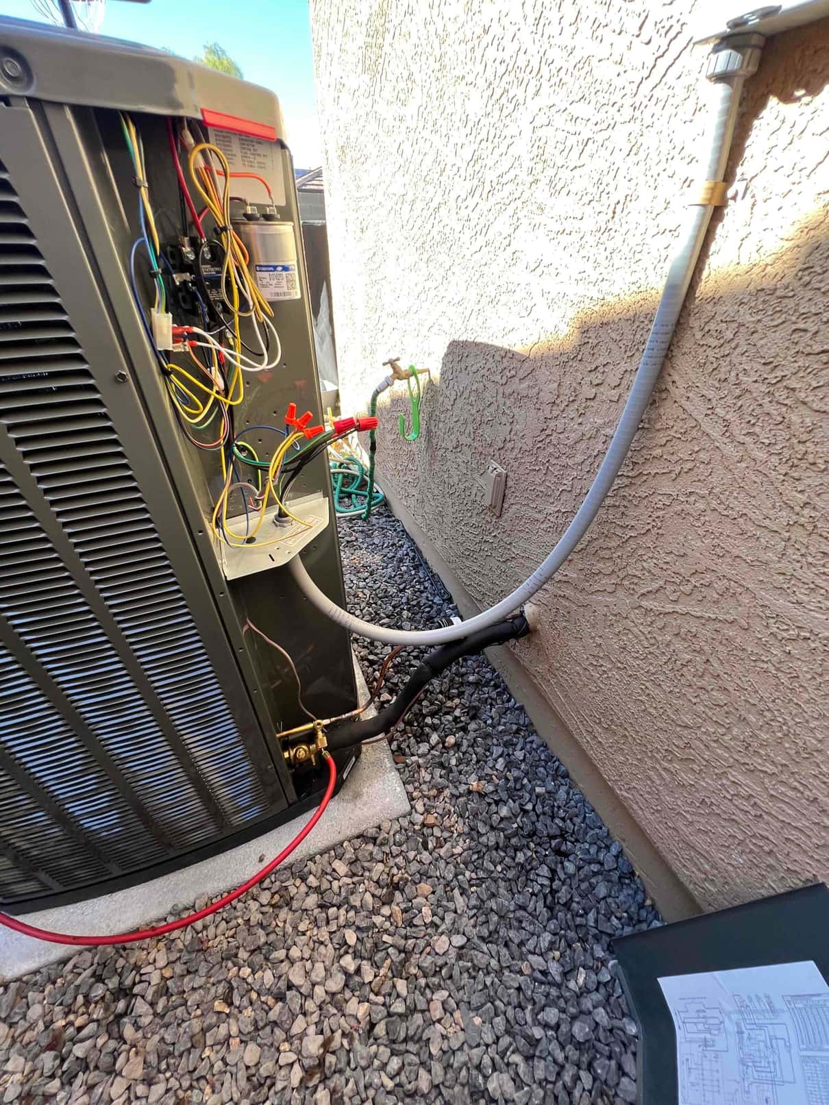 Outdoor condenser set on a level pad with insulated refrigerant lines, electrical whip, and open control compartment during installation.