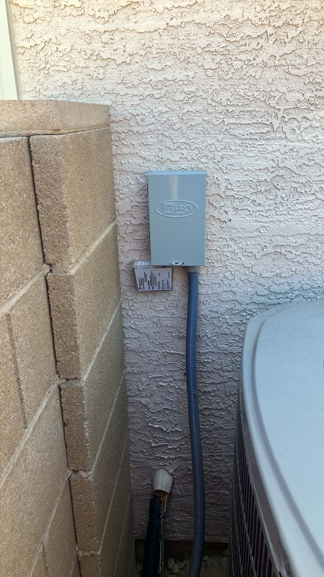 Outdoor disconnect box and flexible conduit installed beside the new condenser, with insulated refrigerant line and wall penetration sealed.