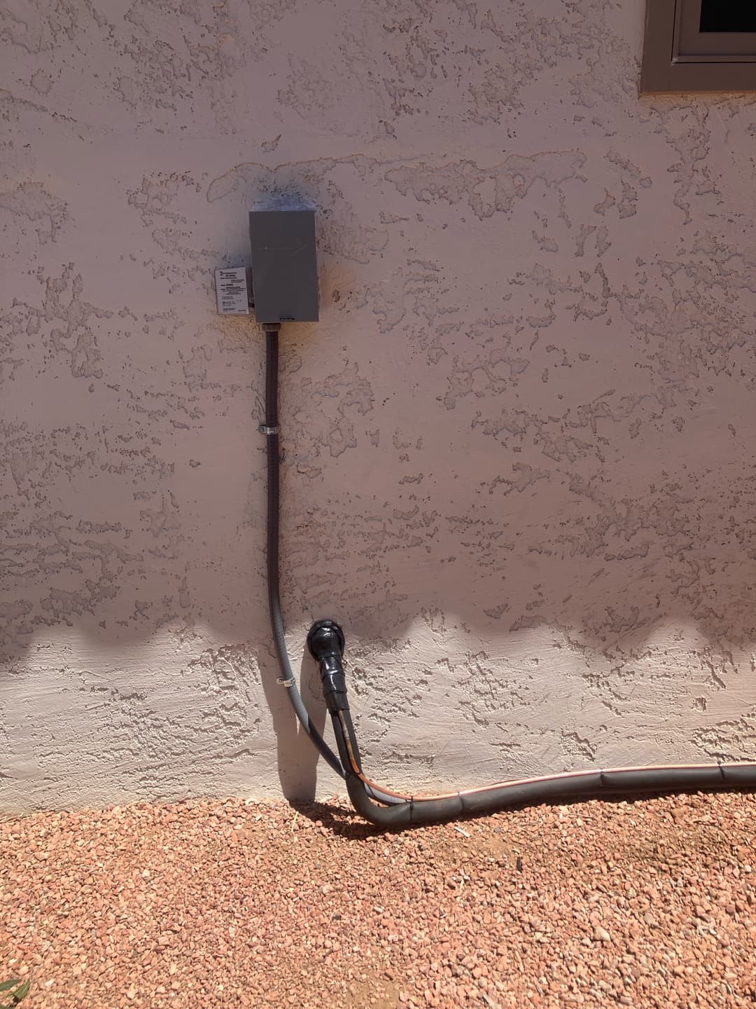 Outdoor disconnect with sealed conduit and insulated refrigerant line set routed along the exterior wall on a gravel base.