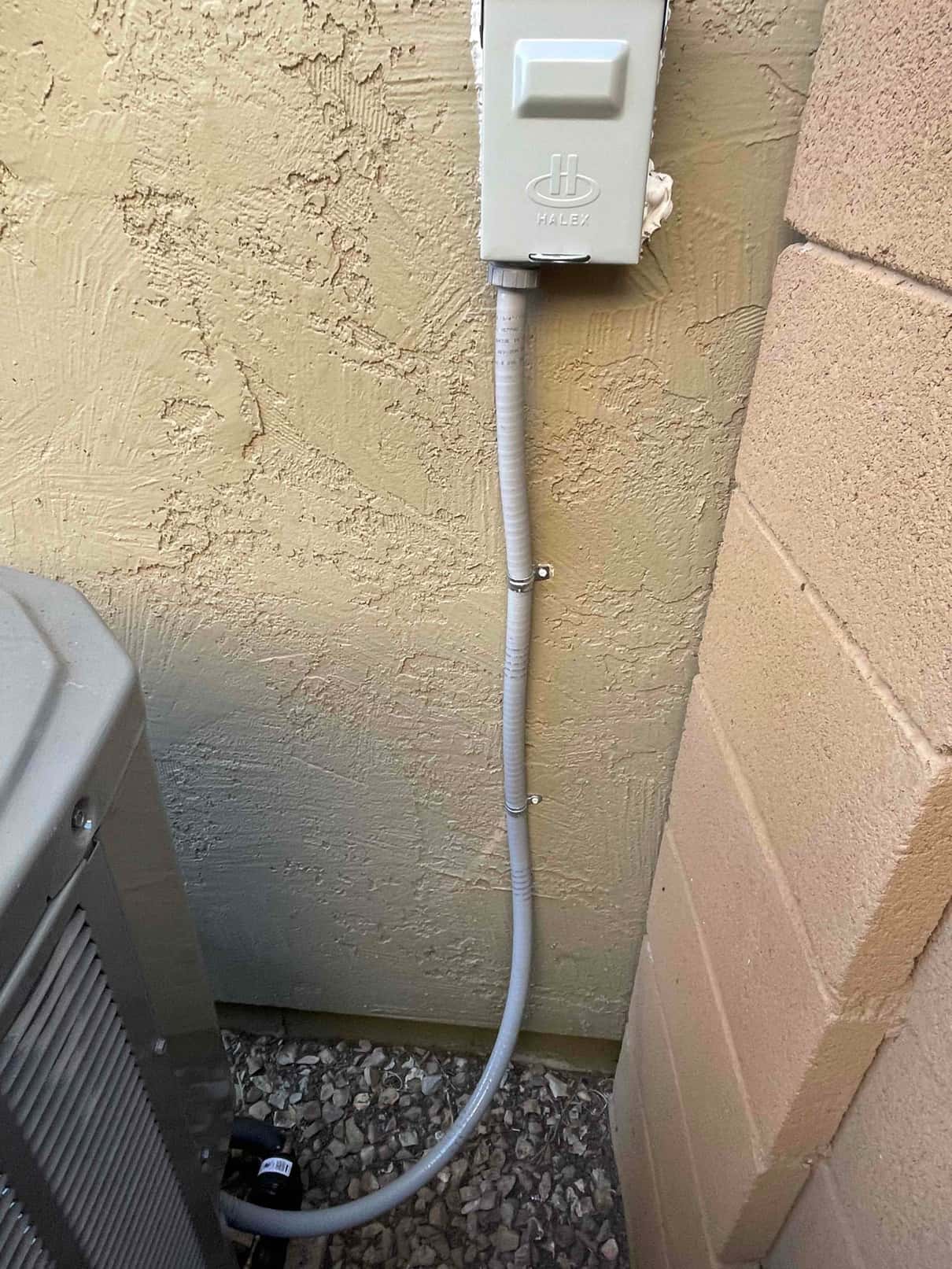 Outdoor electrical disconnect with sealed conduit neatly routed to the new condenser unit, secured against the exterior wall.