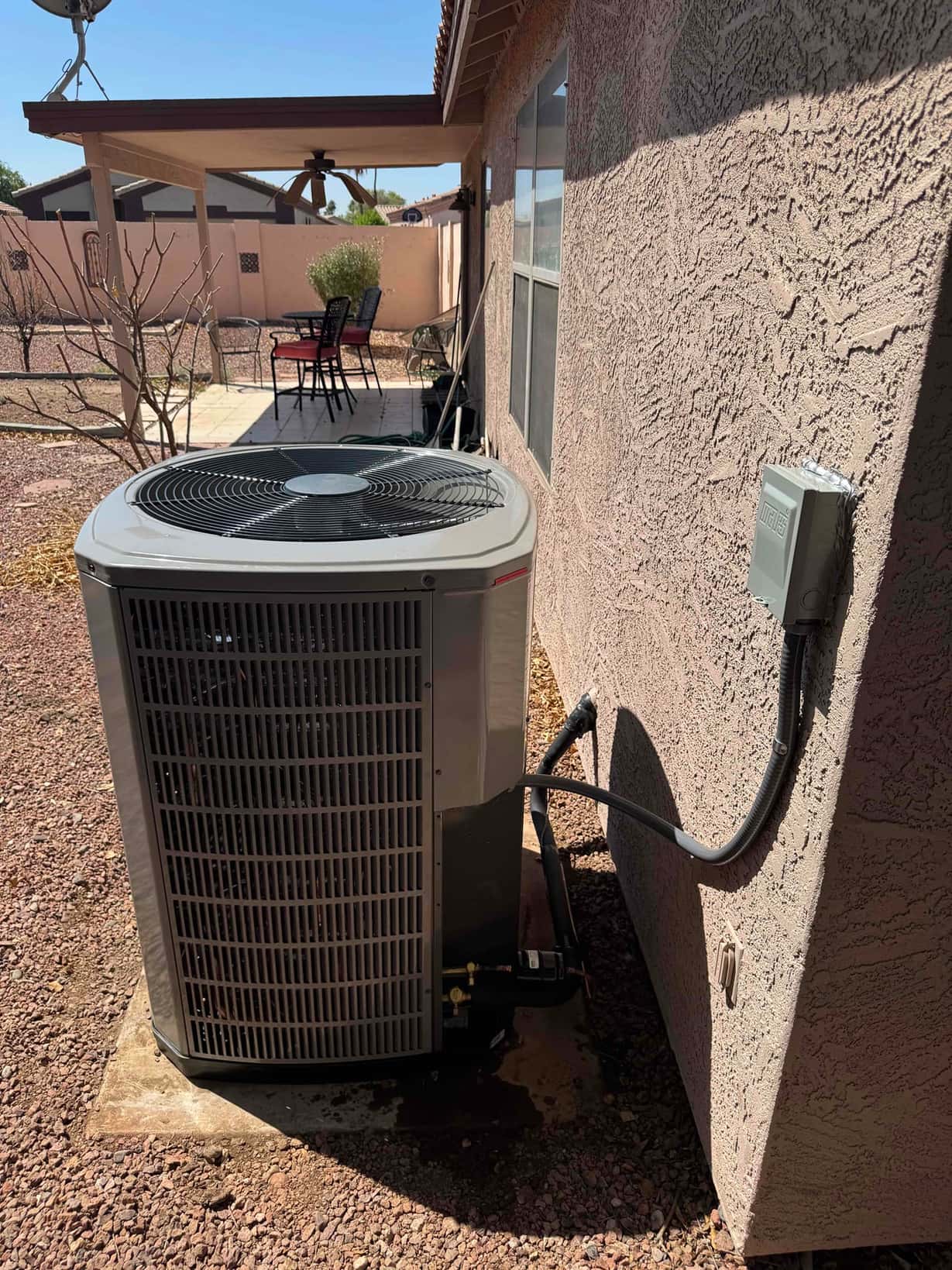 Outdoor heat pump condenser set on a concrete pad with insulated line set and weatherproof electrical disconnect mounted on the wall.