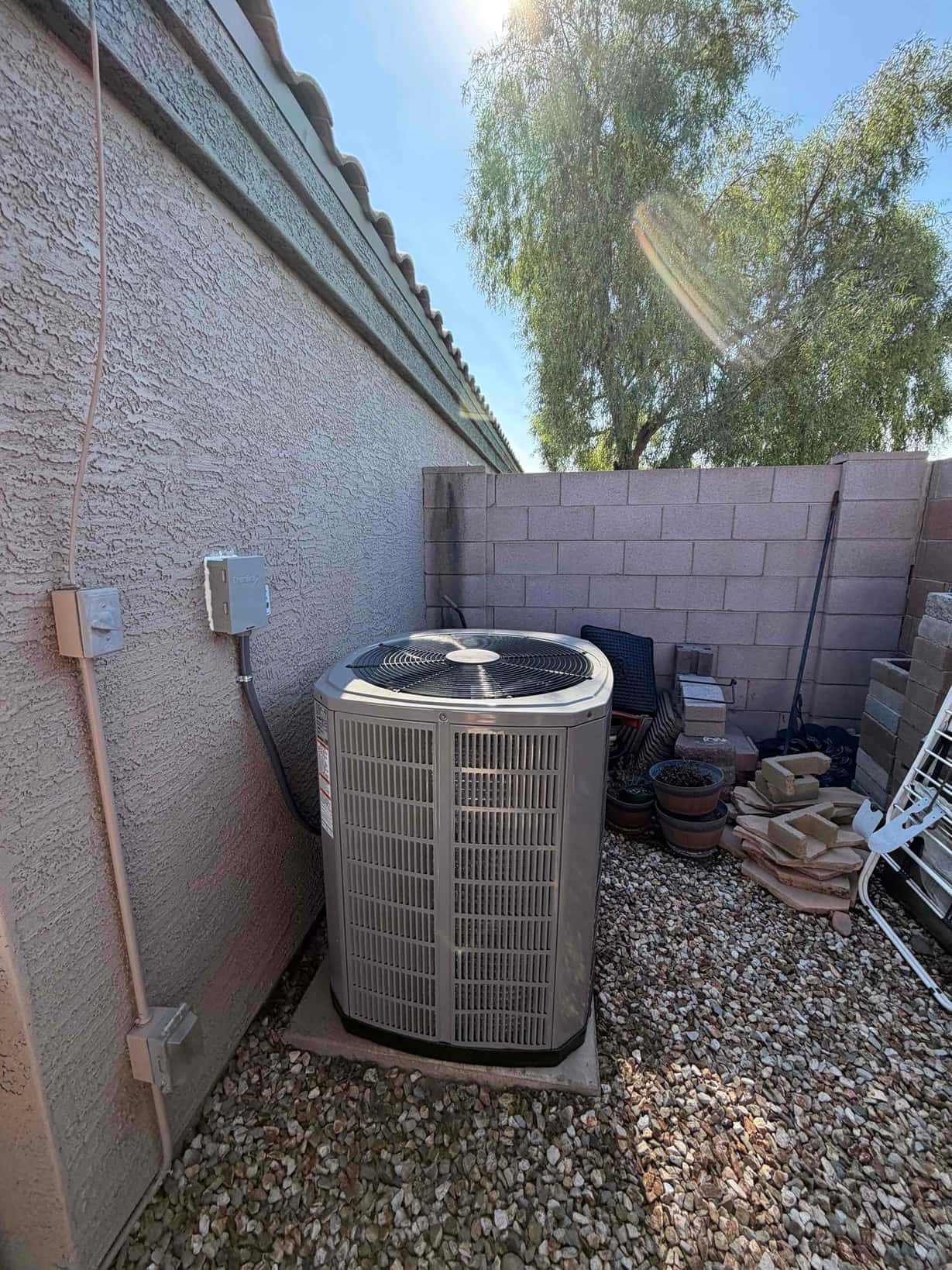 Outdoor heat pump condenser set on a level pad with electrical whip and disconnect mounted on the wall.