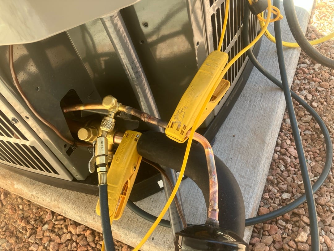 Refrigerant line connections at the outdoor condenser with service ports and hoses attached during installation on a level pad.